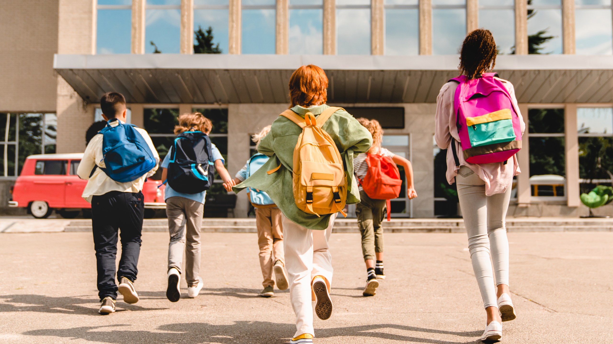 Little kids schoolchildren pupils students running hurrying to the school building for classes lessons from to the school bus. Welcome back to school. The new academic semester year start