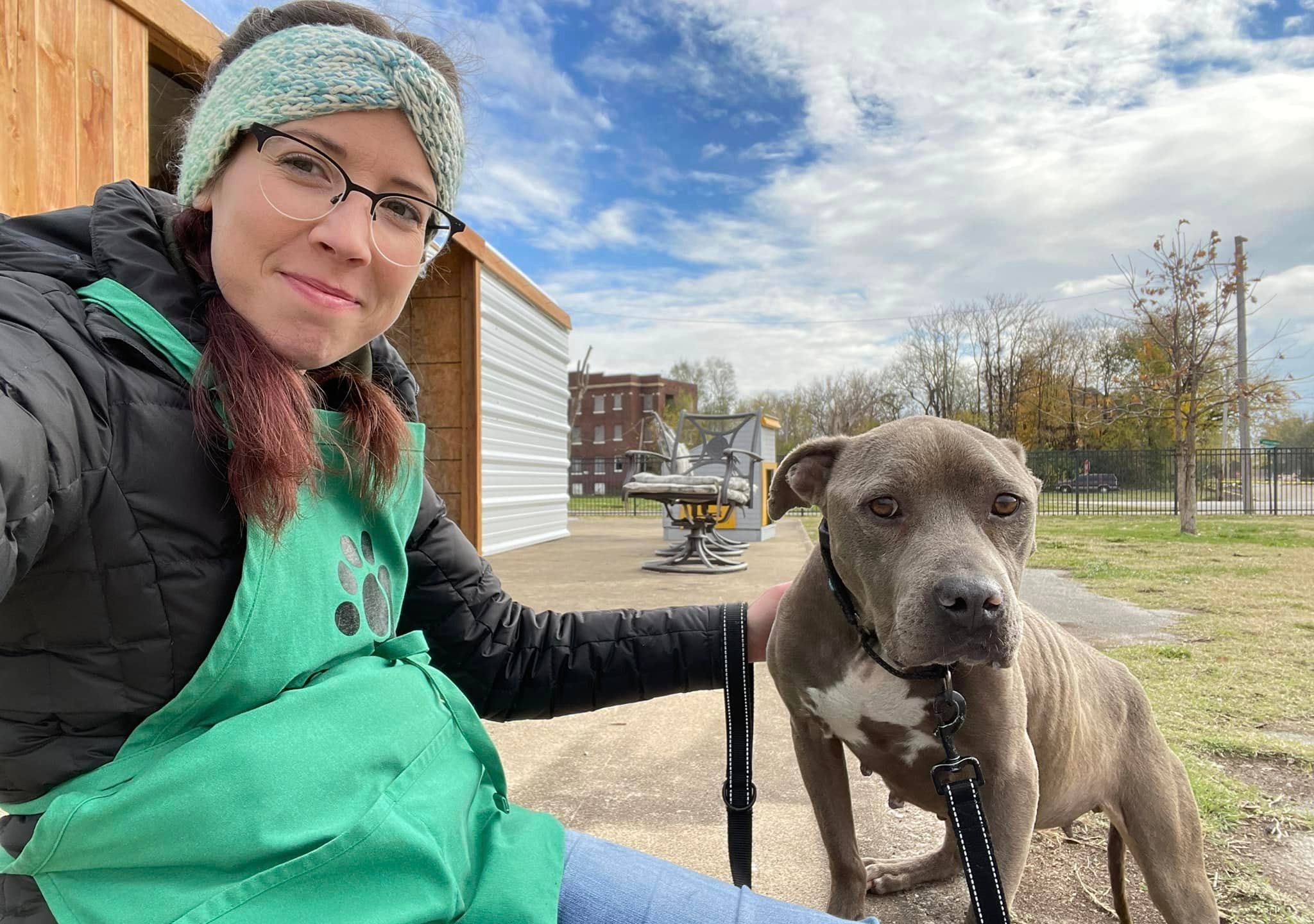 A woman sits with a grey pitbull dog outside