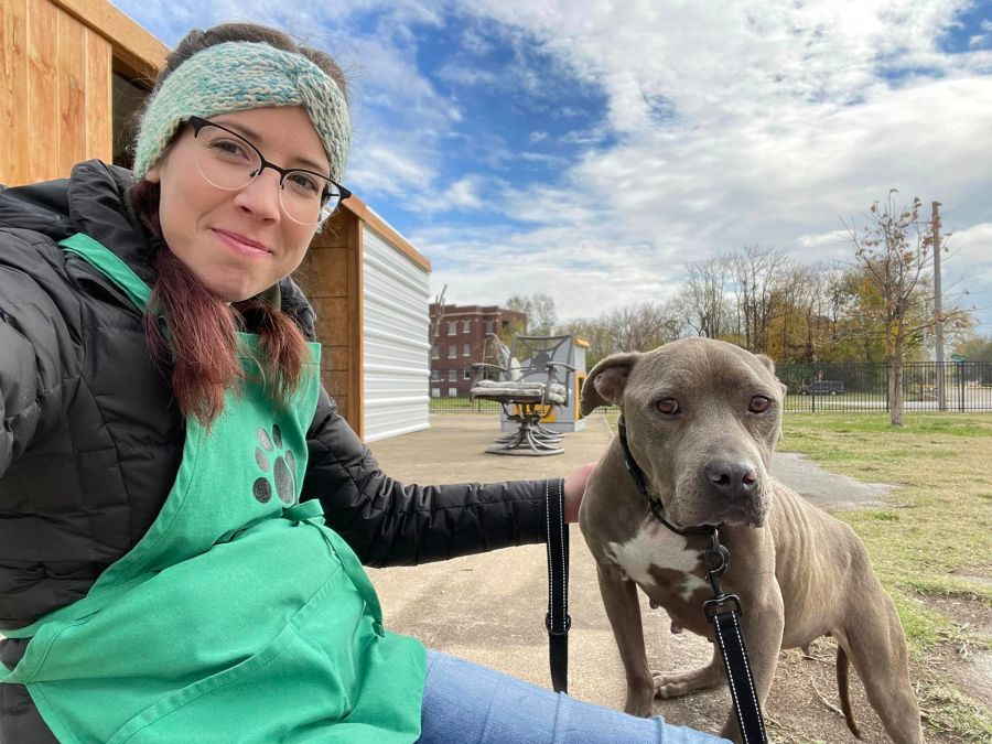 A woman sits with a grey pitbull dog outside