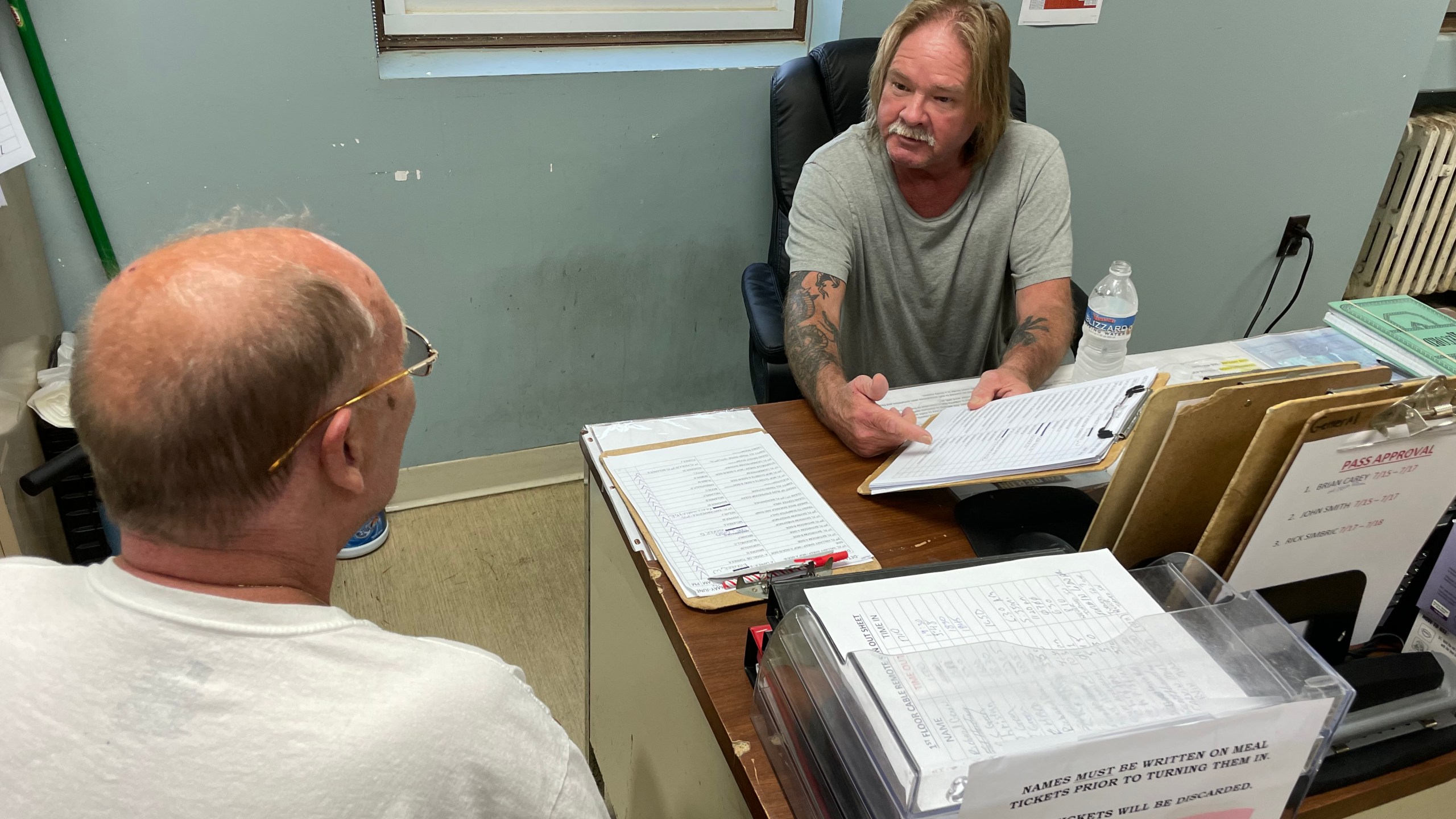 A man holds a clipboard while talking to another man