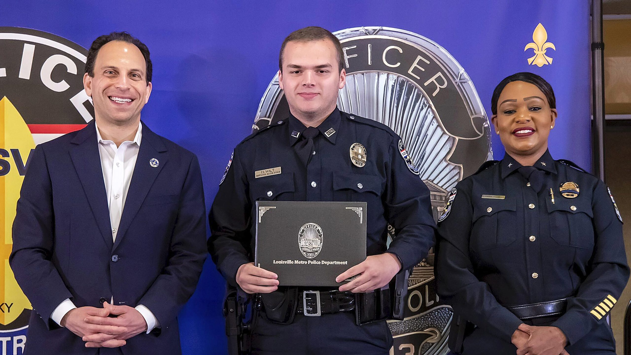 In this photo provided by the Louisville Metro Police Department, from left, Louisville Mayor Craig Greenberg, Officer Nickolas Wilt and Louisville Metro Interim Police Chief Jacquelyn Gwinn-Villaroel pose for a photo, in Louisville, Ky., March 31, 2023. Wilt was shot while responding to a call where a bank employee armed with a rifle opened fire at his workplace early Monday, April 10. (Louisville Metro Police Department via AP)