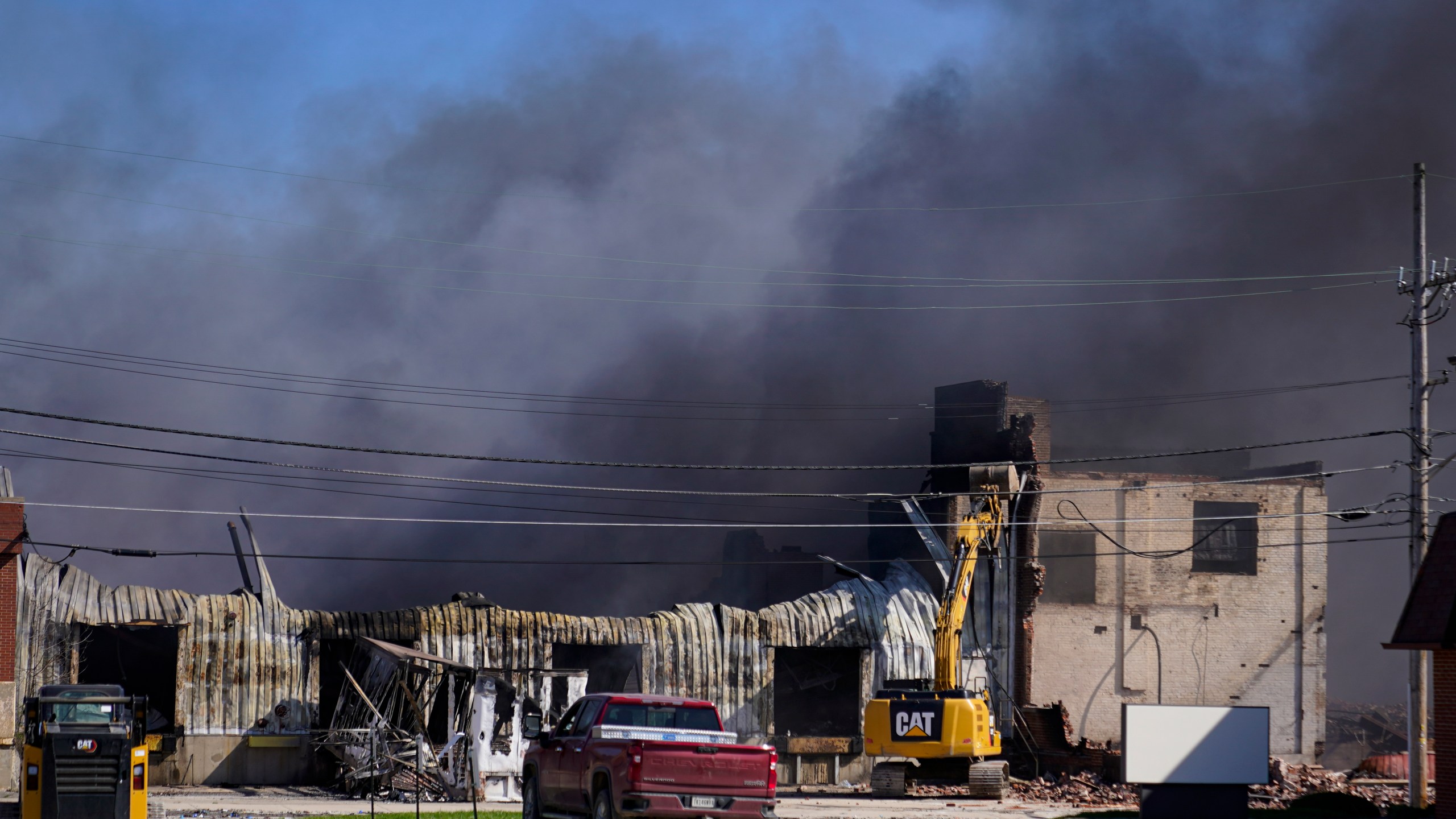 Workers knock down a section of site of an industrial fire the area as smoke billows from the site in Richmond, Ind., Wednesday, April 12, 2023. Authorities urged people to evacuate if they live near the fire. The former factory site was used to store plastics and other materials for recycling or resale. (AP Photo/Michael Conroy)