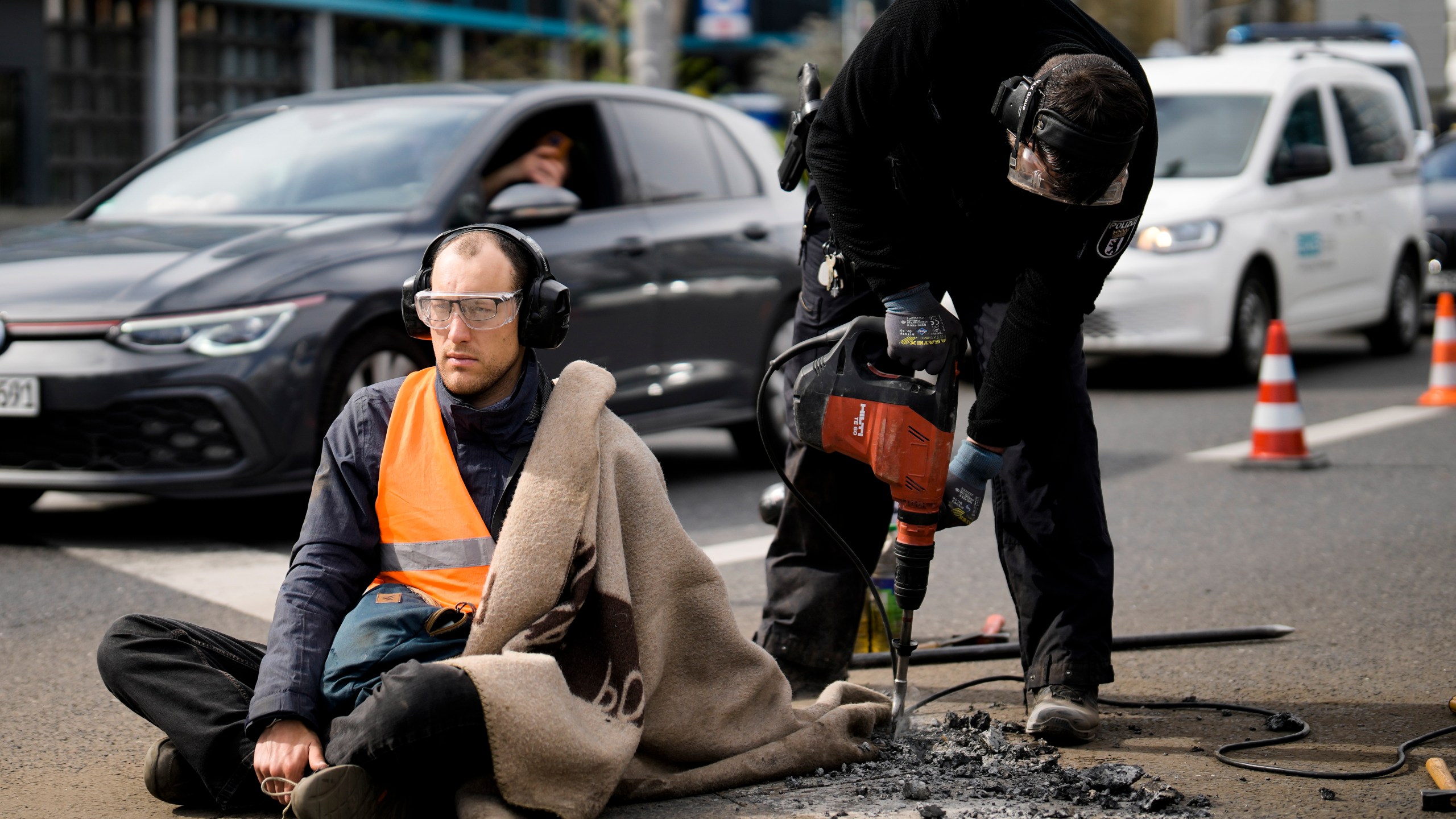 Police removes the pavement next to the hand of a climate activist during a protest against the climate policy of the German government in Berlin, Germany, Monday, April 24, 2023. German climate activists tried bringing traffic to a standstill in Berlin on Monday morning by gluing themselves to streets all over the capital. (AP Photo/Markus Schreiber)