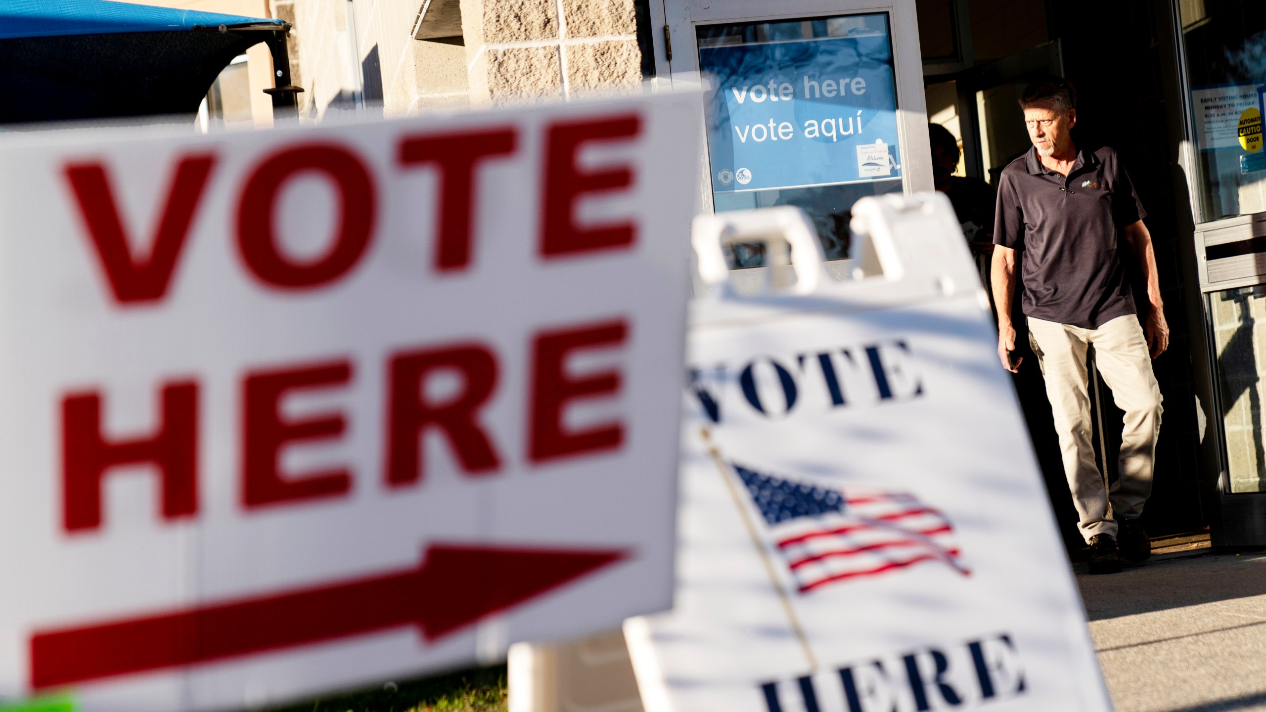 FILE - Signs point to the entrance on the last day of early voting before the midterm election as a man walks out of a polling site in Cranston, R.I., on Nov. 7, 2022. Almost half of all voters in the 2022 midterm elections cast their ballots before Election Day either by mail or through early voting, with Asian and Hispanic voters leading the way, new data from the U.S. Census Bureau released Tuesday, May 2, 2023, shows, even as Republican-led states have tightened rules on voting by mail. (AP Photo/David Goldman, File)