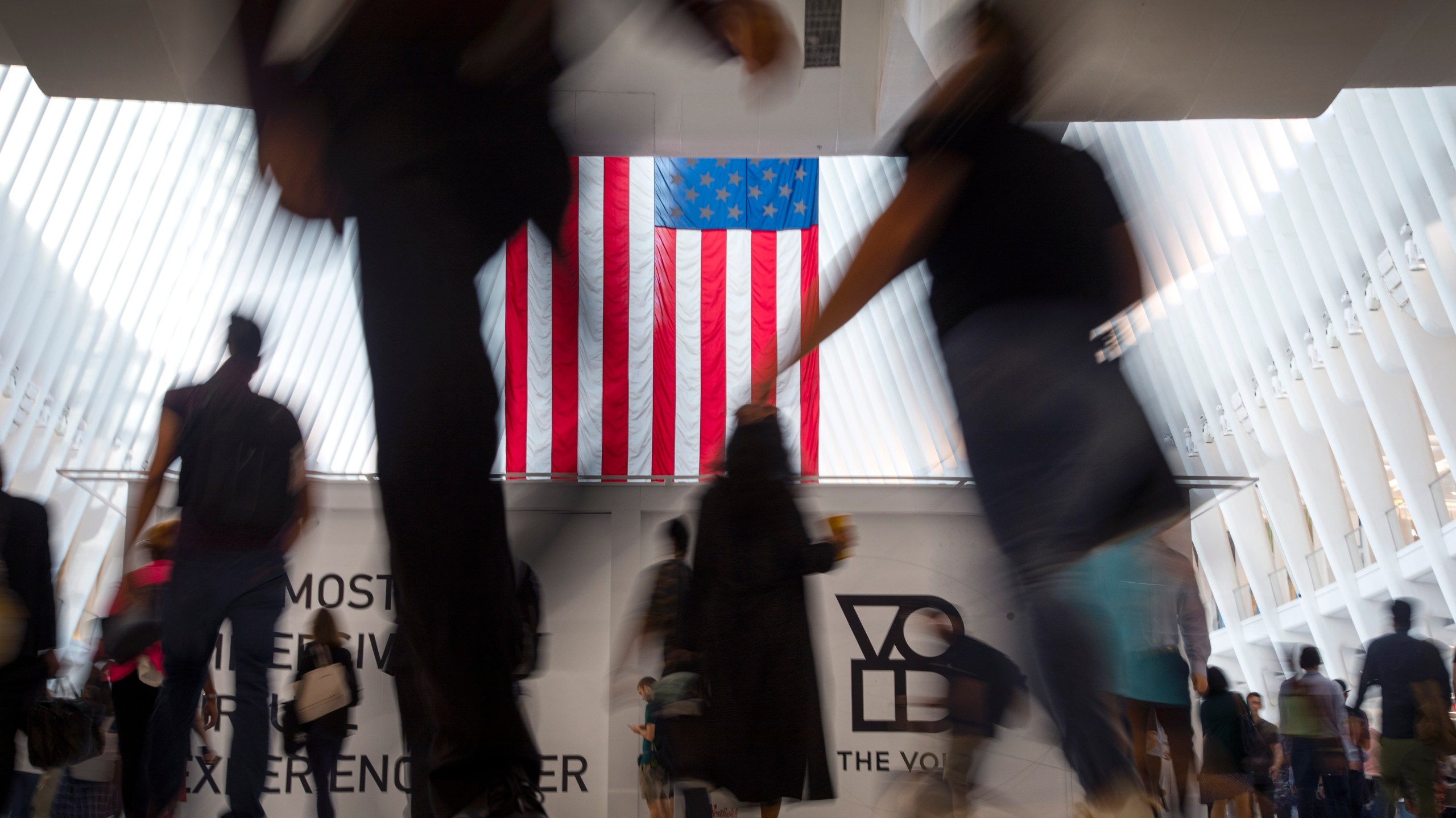 FILE - People walk past an American flag inside the Oculus, part of the World Trade Center transportation hub, at the start of a work day in New York, Sept. 11, 2019. American lore is full of tales of a nation built on the foundations of individualism. In reality, loneliness in America can be deadly. In May 2023, the U.S. surgeon general declared it an epidemic, saying that it takes as deadly a toll as smoking. (AP Photo/Wong Maye-E, File)