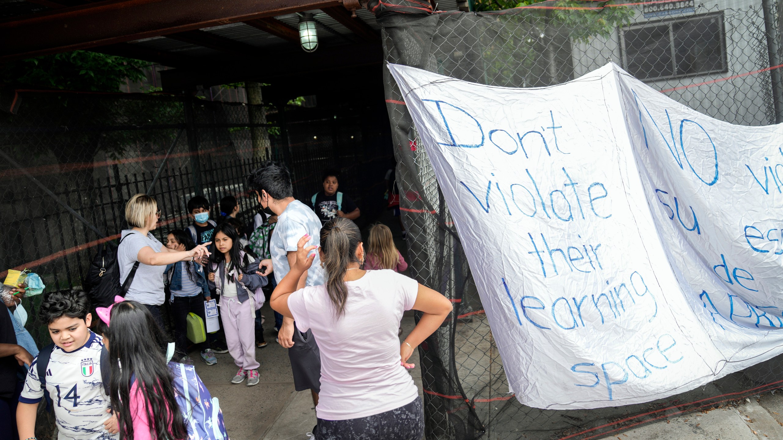 Students exit P.S. 172 after classes end for the day as a protest sign is displayed outside the school, Tuesday, May 16, 2023, in New York. New York City Mayor Eric Adam's plan to temporarily house immigrants in the school's gymnasium has frustrated some community members who protested outside the building earlier in the day. (AP Photo/John Minchillo)