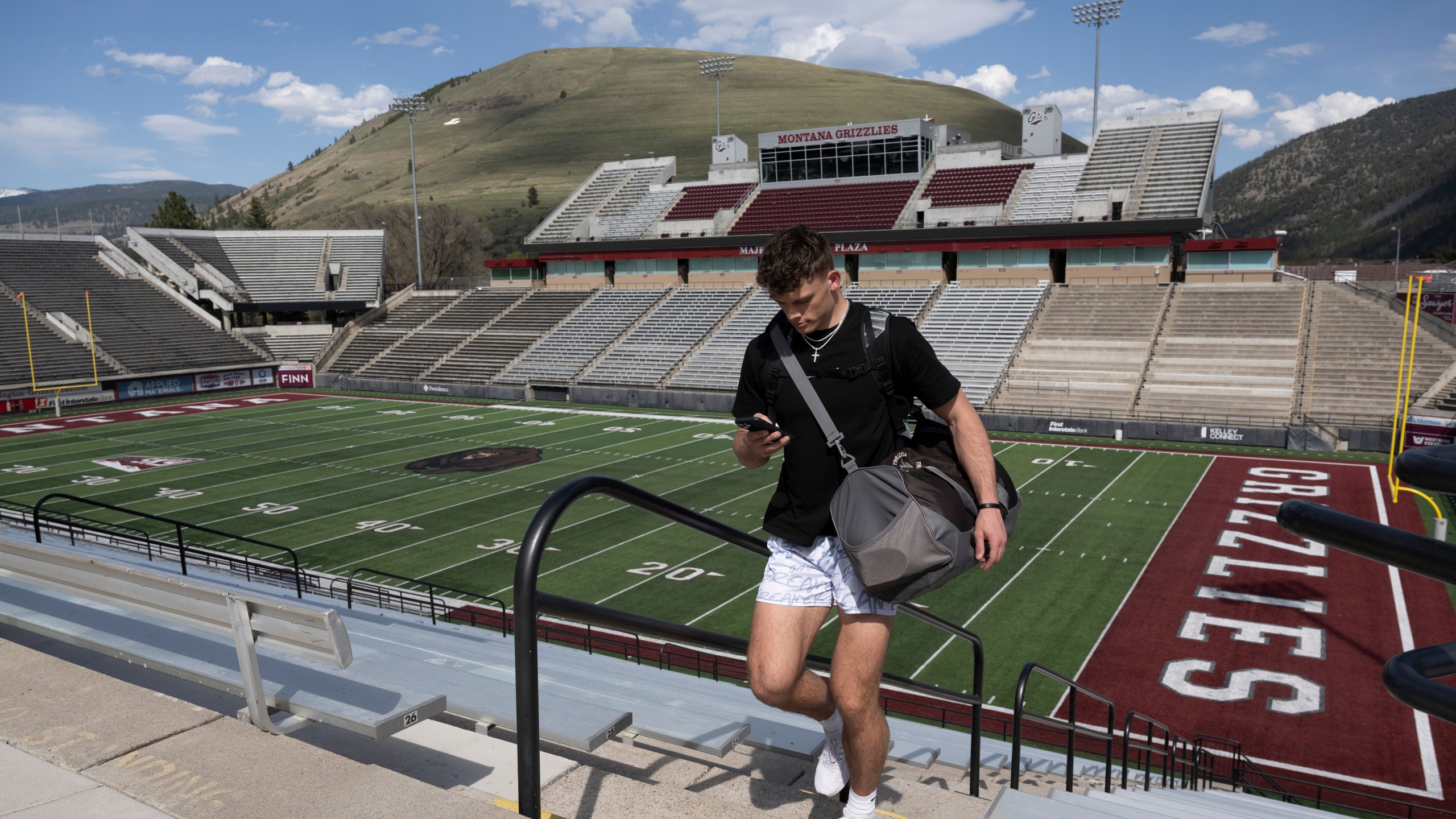 Adam Botkin, a football TikTok influencer, uses his phone after recording a video for a post at Washington-Grizzly Stadium in Missoula, Mont., on Monday, May 1, 2023. Botkin, a former walk-on place kicker and punter for the Montana Grizzlies, gained notoriety on the social media platform after videos of him performing kicking tricks went viral. (AP Photo/Tommy Martino)