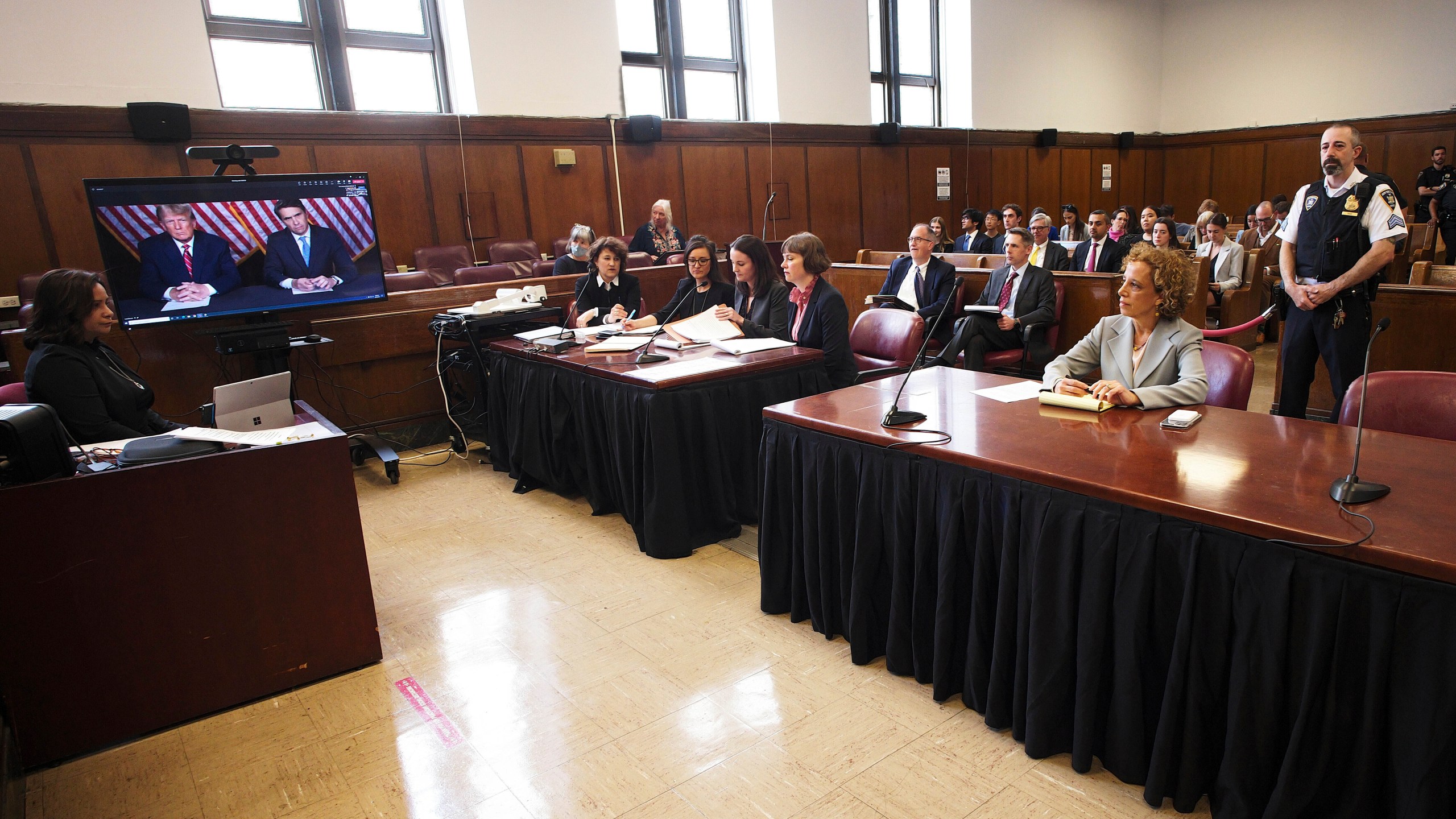 Former president Donald Trump, left on screen, and his attorney, Todd Blanche, right on screen, appear by video, as his other attorney Susan Necheles, right, looks on, before a hearing begins in Manhattan criminal court, in New York, Tuesday, May 23, 2023. Trump made a video appearance Tuesday in his New York criminal case, with the judge tentatively setting a trial date for late March of next year. (AP Photo/Curtis Means via Pool)