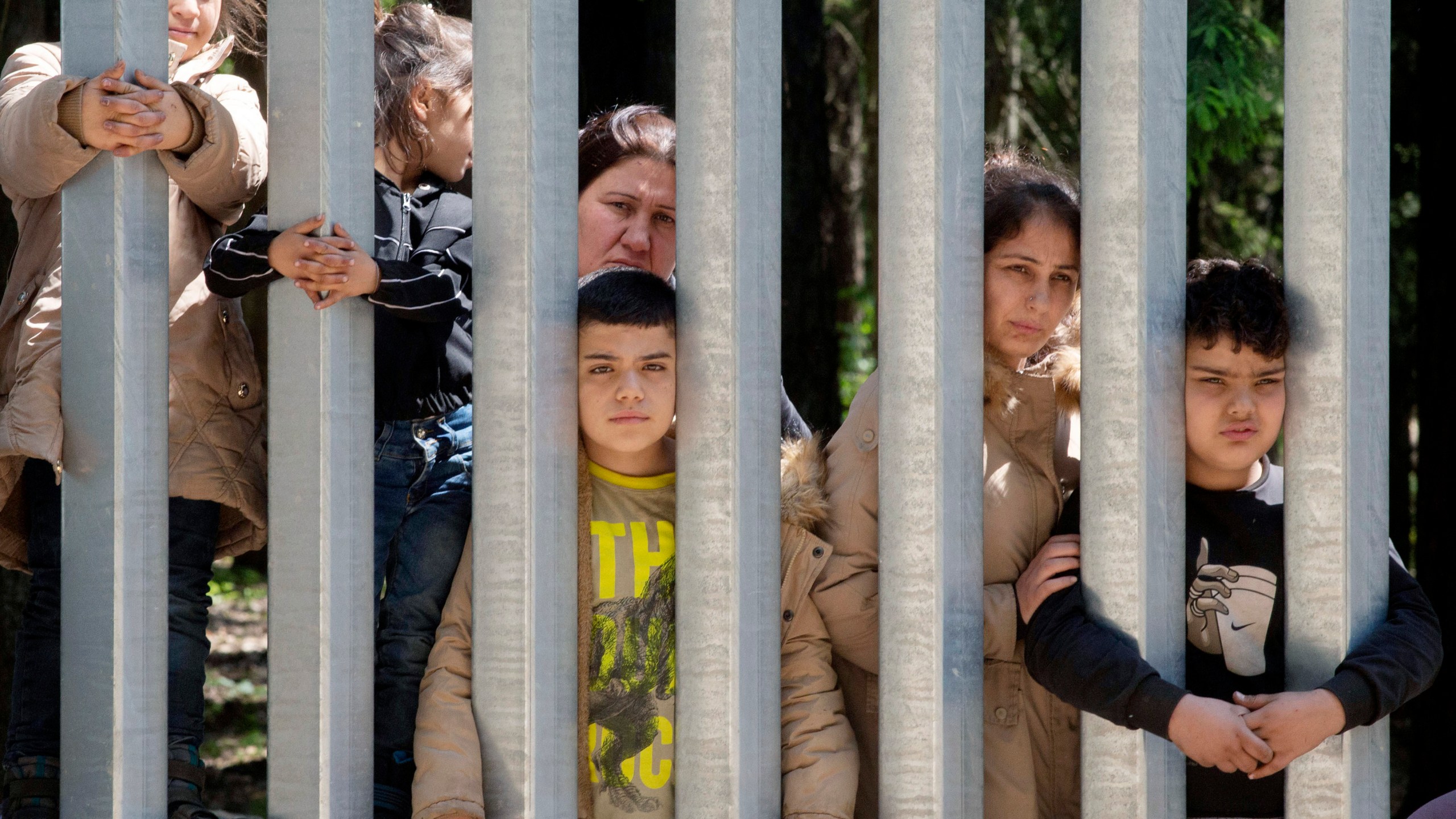 Members of a group of some 30 migrants seeking asylum are seen in Bialowieza, Poland, on Sunday, 28 May 2023 across a wall that Poland has built on its border with Belarus to stop massive migrant pressure. The group has remained stuck at the spot for three days, according to human rights activists. (AP Photo/Agnieszka Sadowska)