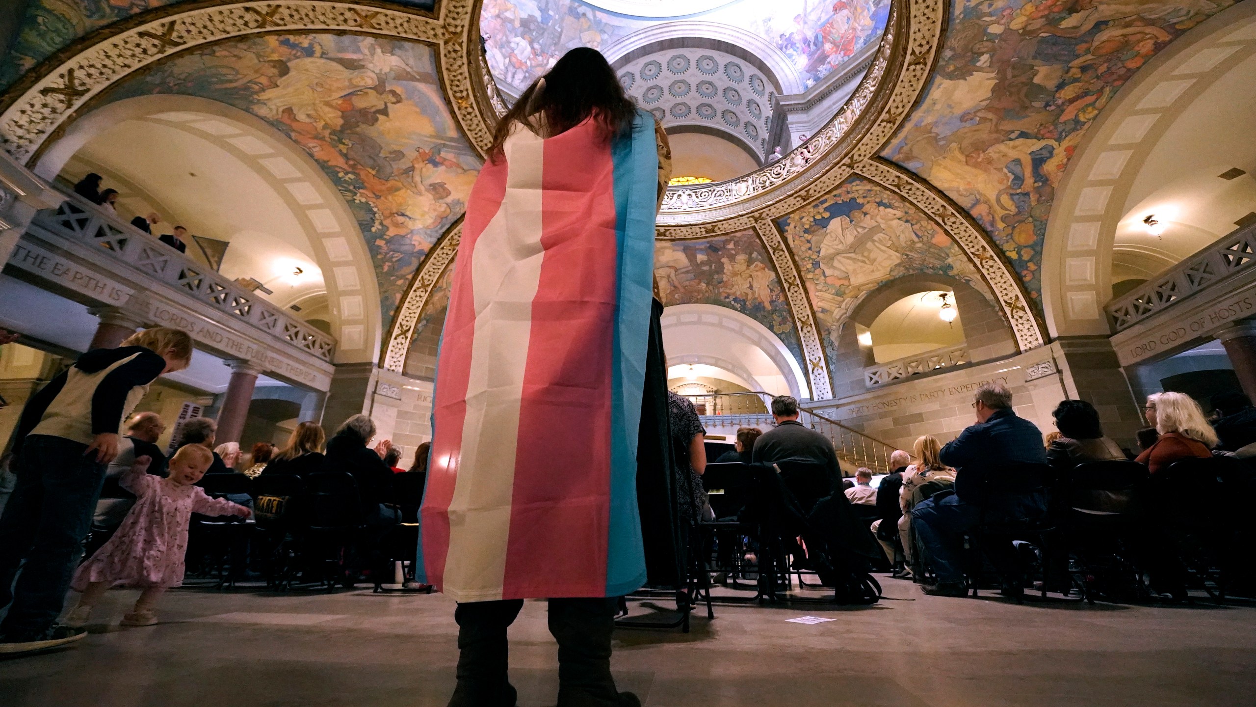 FILE - Glenda Starke wears a transgender flag as a counter protest during a rally in favor of a ban on gender-affirming health care legislation, March 20, 2023, at the Missouri Statehouse in Jefferson City, Mo. Transgender minors and some adults in Missouri will soon be banned from accessing puberty blockers, hormones and gender-affirming surgeries under a bill signed Wednesday, June 7, 2003, by the state's Republican governor. (AP Photo/Charlie Riedel, File)