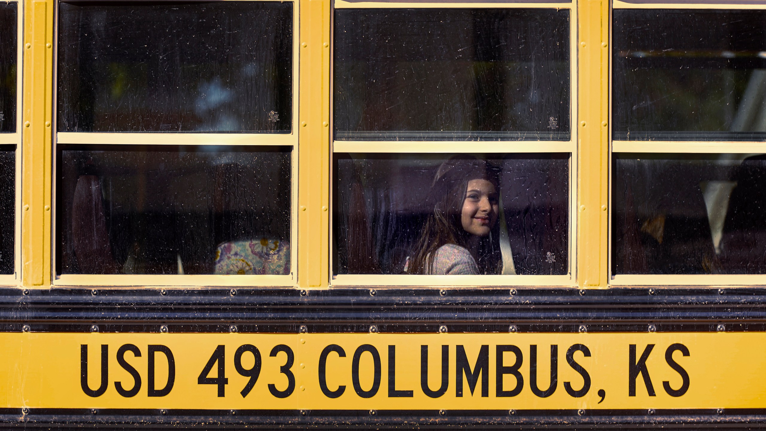 Third-grader Lucy Perry waits on a bus after classes at Highland Elementary School in Columbus, Kan., on Monday, Oct. 17, 2022. Third graders in the tiny 900-student Columbus school district have fought to catch up on reading in the wake of COVID-19 disruptions. (AP Photo/Charlie Riedel)