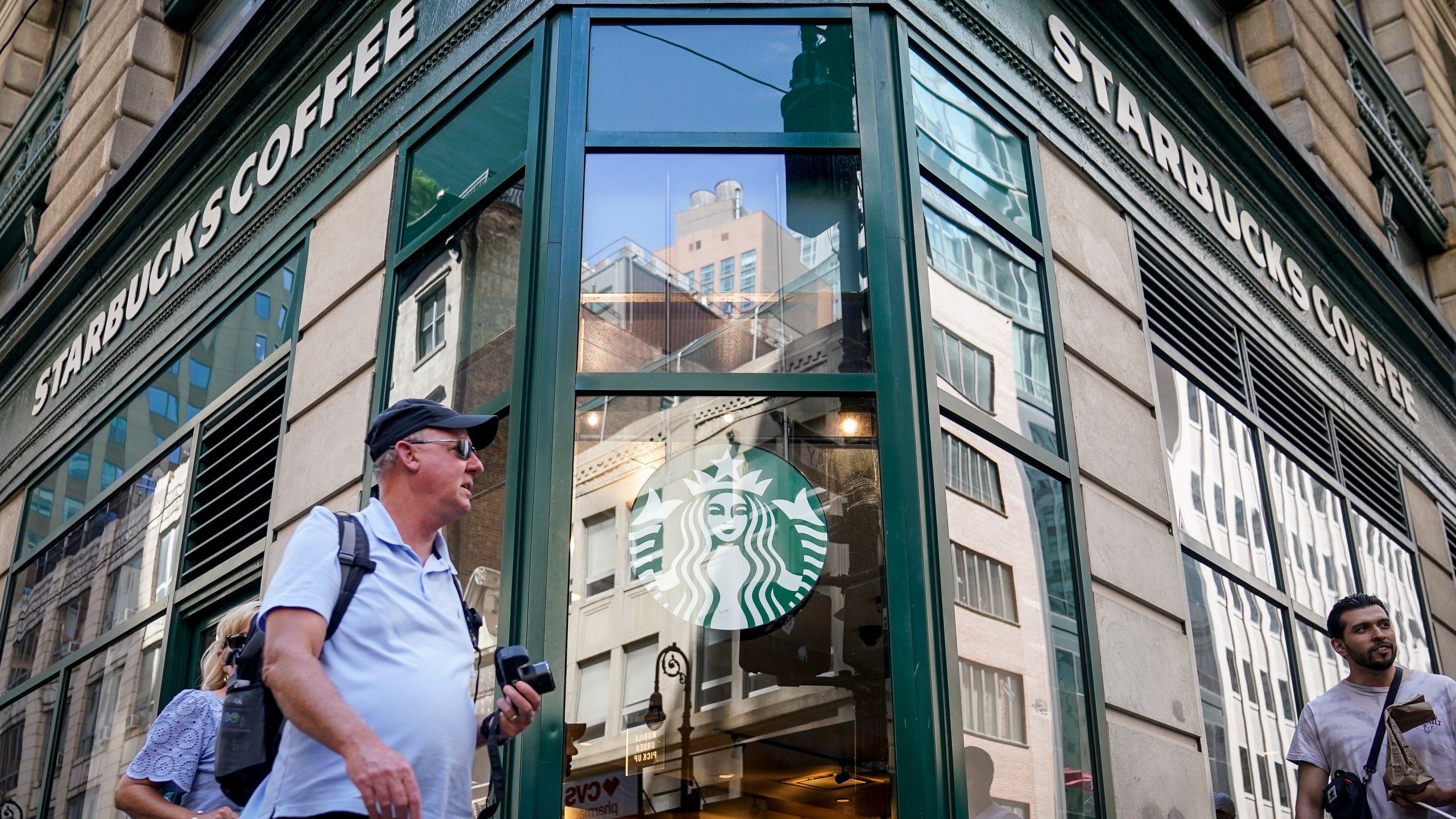 Pedestrians pass a Starbucks in the Financial District of Lower Manhattan, Tuesday, June 13, 2023, in New York. Starbucks is denying union organizers' claims that it banned LGBTQ+ Pride displays in its U.S. stores after Target and other brands experienced backlash. The Seattle coffee giant says there has been no change to its policy and it encourages store leaders to celebrate Pride in June. (AP Photo/John Minchillo)