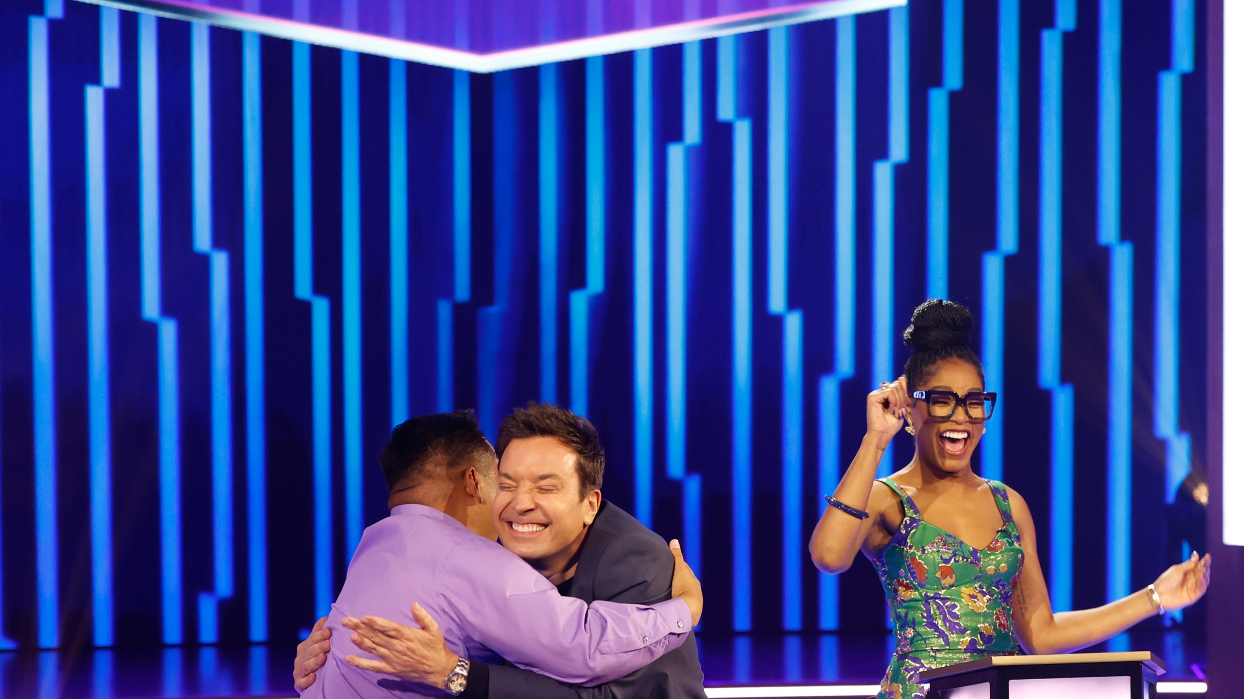 This image released by NBC shows Jimmy Fallon, center, embracing a contestant as host Keke Palmer, looks on, during the game show "Password." (Jordin Althaus/NBC via AP)