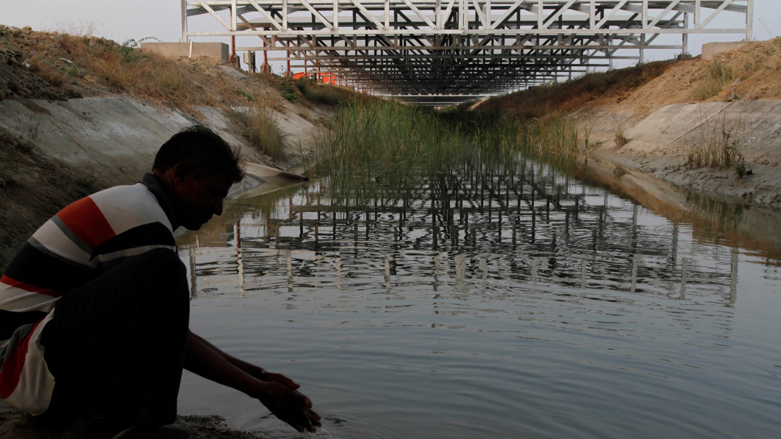 FILE - A worker washes his hands as installed solar panels are visible atop the Narmada canal at Chandrasan village, outside of Ahmadabad, India, Feb. 16, 2012. The project brings water to hundreds of thousands of villages in the dry, arid regions of western India’s Gujarat state. (AP Photo/Ajit Solanki, File)