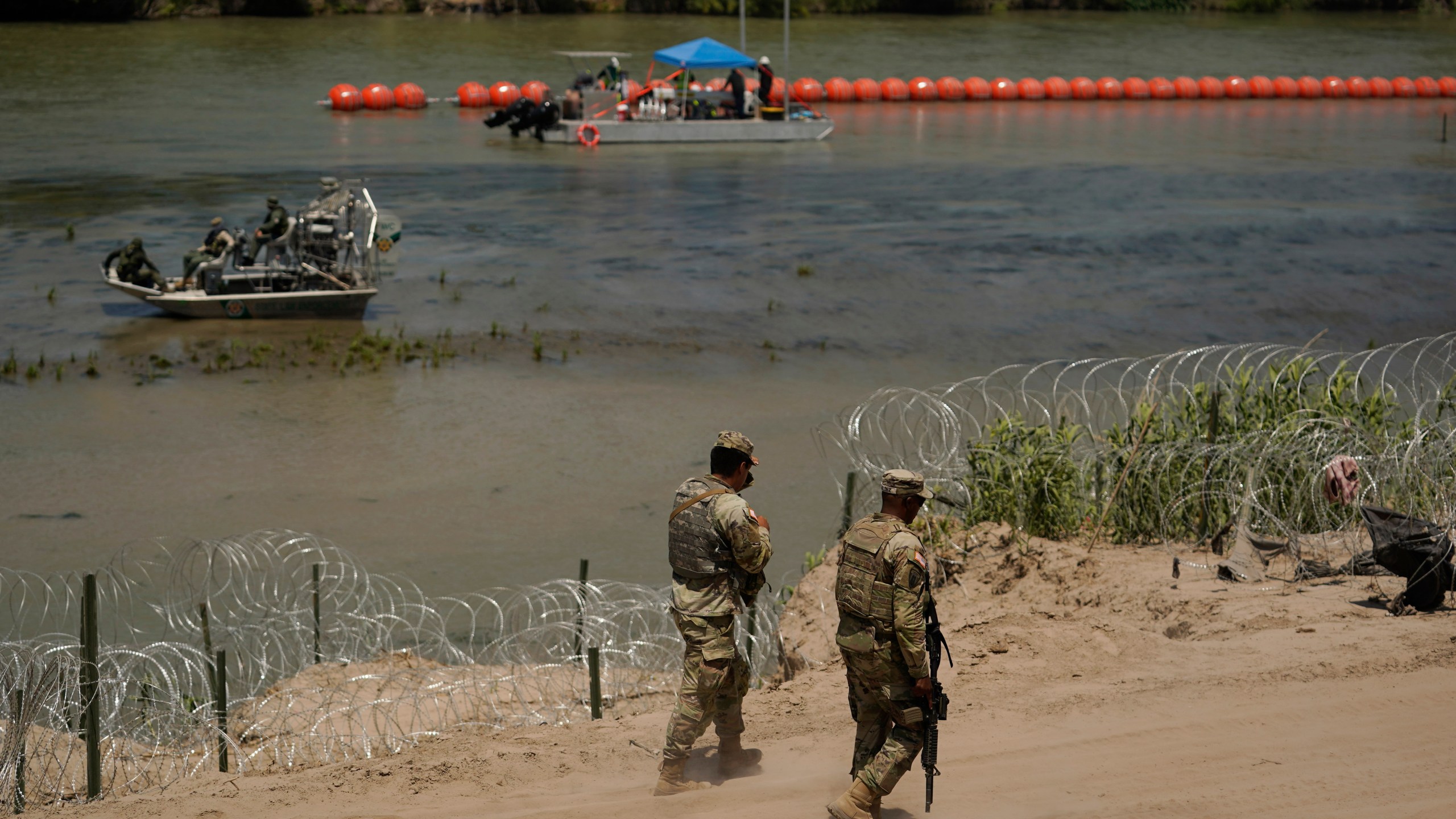 Guardsmen patrol as workers continue to deploy large buoys to be used as a border barrier along the banks of the Rio Grande in Eagle Pass, Texas, Wednesday, July 12, 2023. The floating barrier is being deployed in an effort to block migrants from entering Texas from Mexico. (AP Photo/Eric Gay)