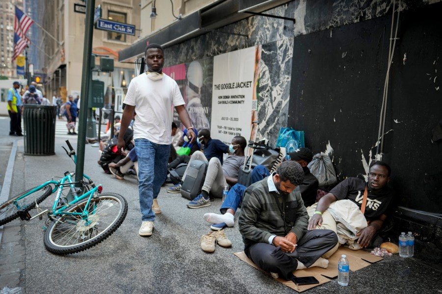 Migrants sit in a queue outside of The Roosevelt Hotel that is being used by the city as temporary housing, Monday, July 31, 2023, in New York. (AP Photo/John Minchillo)