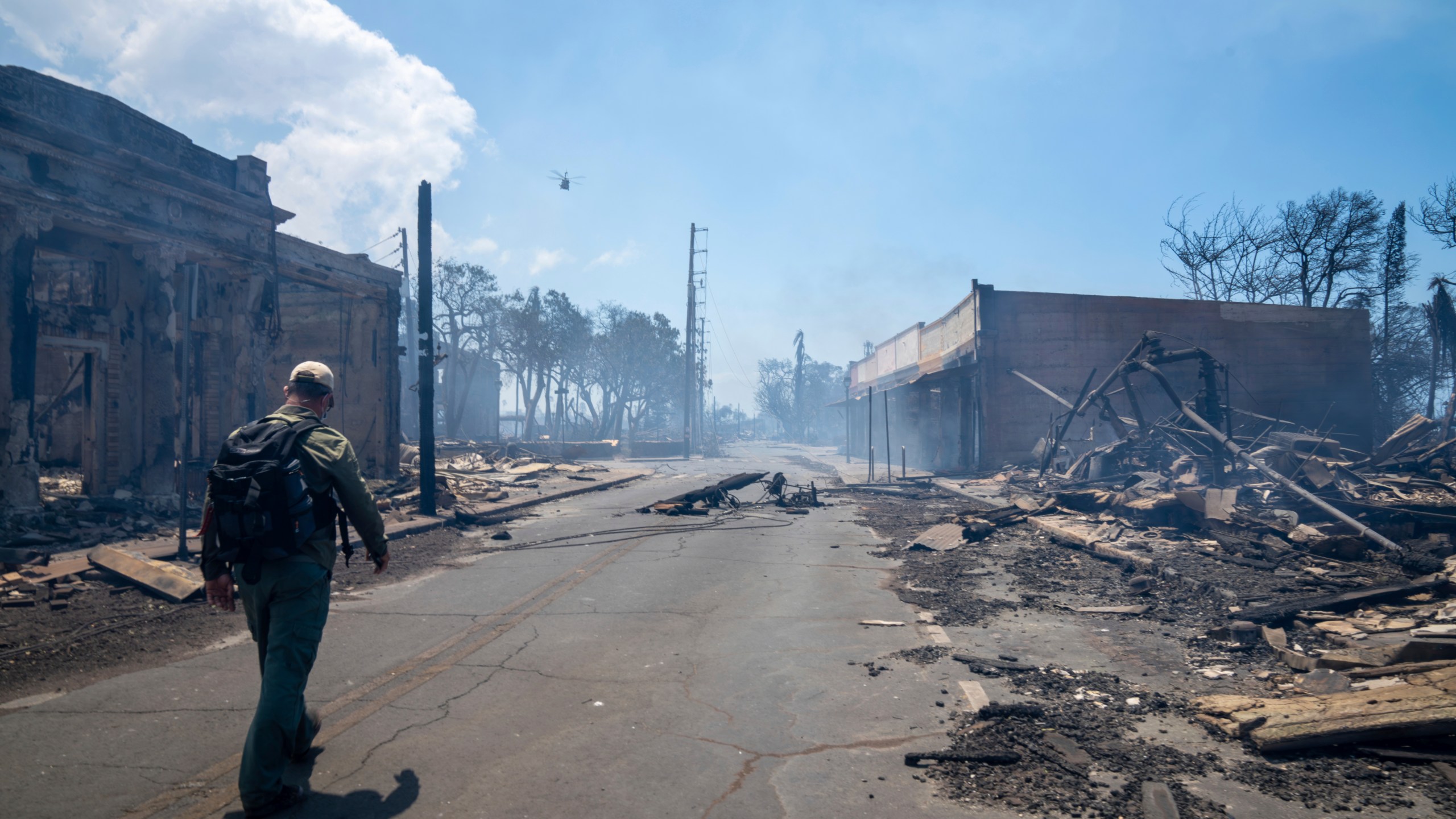 In this photo provided by Tiffany Kidder Winn, a man walks past wildfire wreckage on Wednesday, Aug. 9, 2023, in Lahaina, Hawaii. The scene at one of Maui's tourist hubs on Thursday looked like a wasteland, with homes and entire blocks reduced to ashes as firefighters as firefighters battled the deadliest blaze in the U.S. in recent years. (Tiffany Kidder Winn via AP)