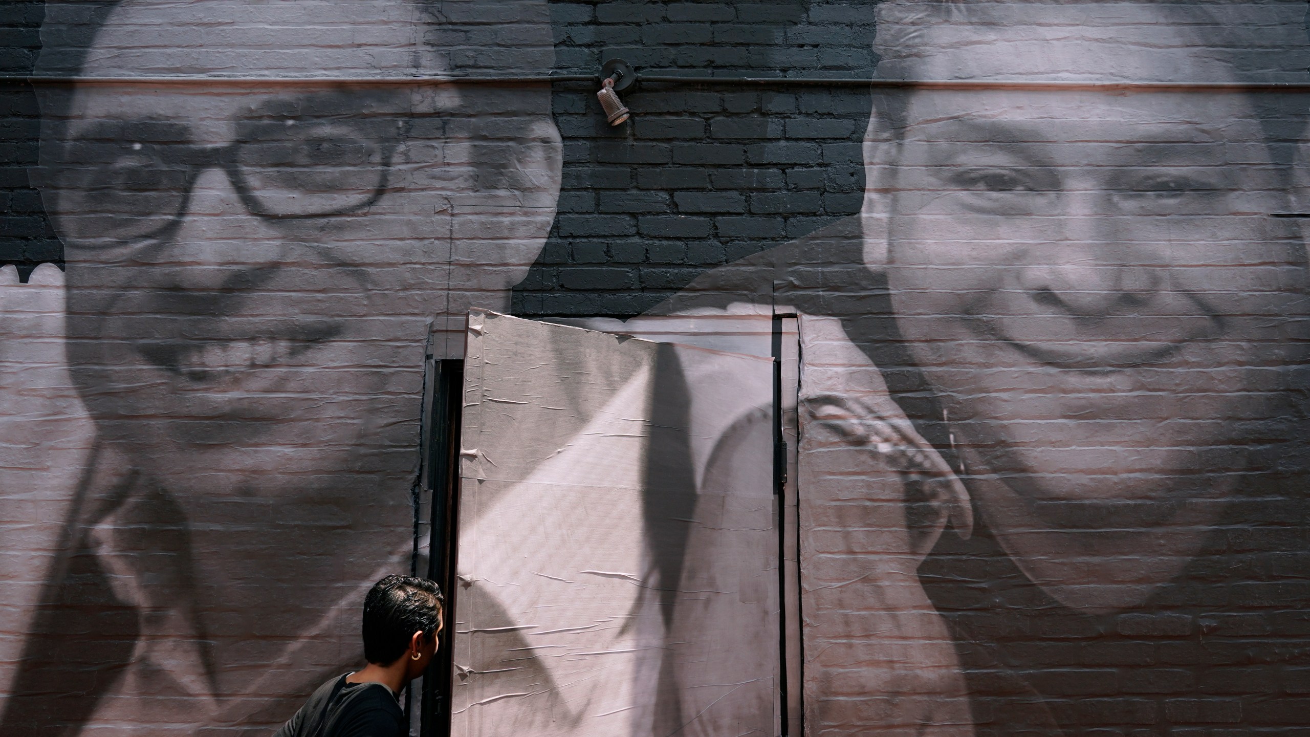 FILE - A woman steps through a door that is covered by a mural depicting American hostages and wrongful detainees who are being held abroad, Wednesday, July 20, 2022, in the Georgetown neighborhood of Washington. At left is Siamak Namazi, who has been in captivity in Iran since 2015. At right is Jose Angel Pereira, who has been imprisoned in Venezuela since 2017. Iran has transferred five Iranian-Americans from prison, identifying three of the prisoners as Siamak Namazi, Emad Shargi, and Morad Tahbaz, to house arrest. The move comes after Tehran has spent months suggesting a prisoner swap with Washington. (AP Photo/Patrick Semansky, File)