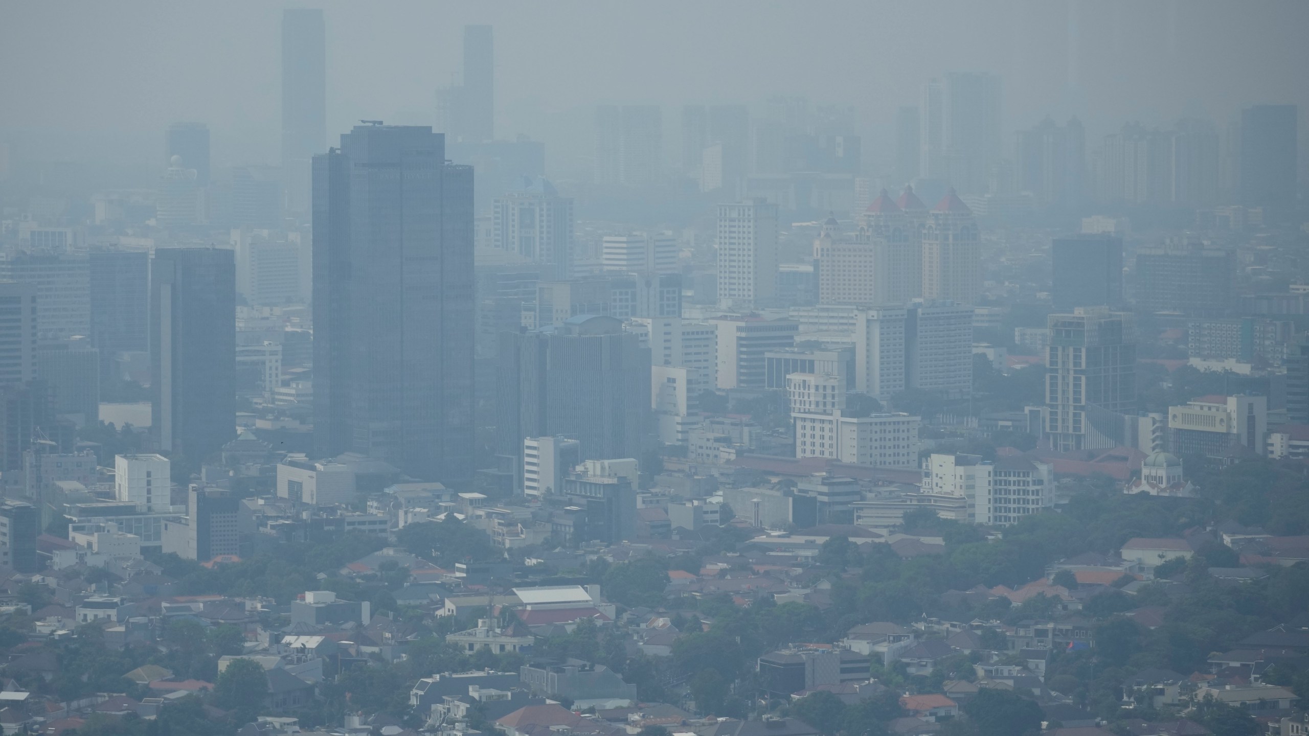 FILE - Haze blankets the main business district in Jakarta, Indonesia, Aug. 11, 2023. The world’s corporations produce so much climate change pollution, it could eat up about 44% of their profits if they had to pay damages for what they spew, according to a study on Thursday, Aug. 24, by economists of nearly 15,000 public companies. (AP Photo/Dita Alangkara, File)