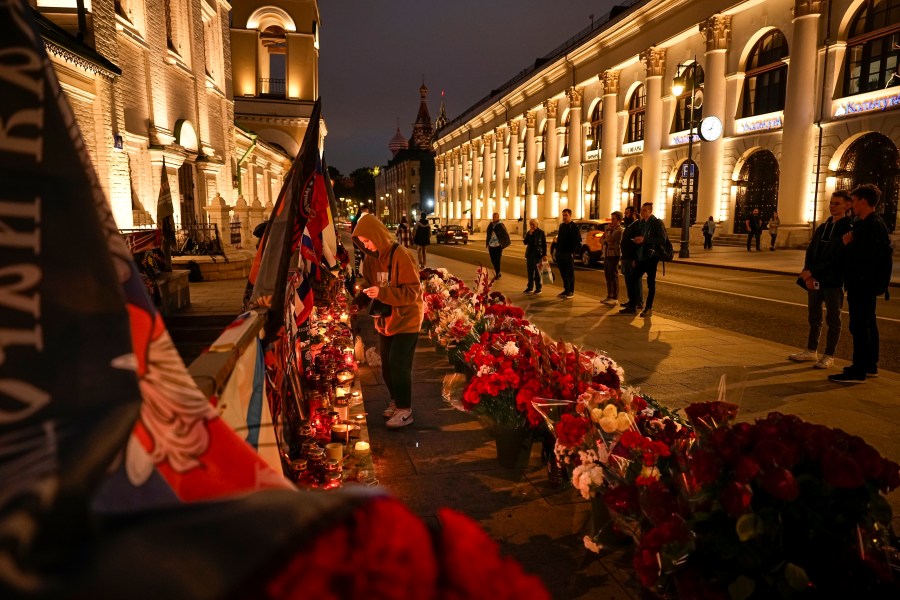 A young woman lights a candle as others stand at an informal street memorial with flowers and lit candles for Wagner Group's military group members killed in a plane crash, near the Kremlin, in the background, in Moscow, Russia, Tuesday, Aug. 29, 2023. The Kremlin says Russian President Vladimir Putin isn't planning to attend the funeral of Yevgeny Prigozhin, who died last week in a plane crash two months after launching his brief rebellion. (AP Photo/Alexander Zemlianichenko)