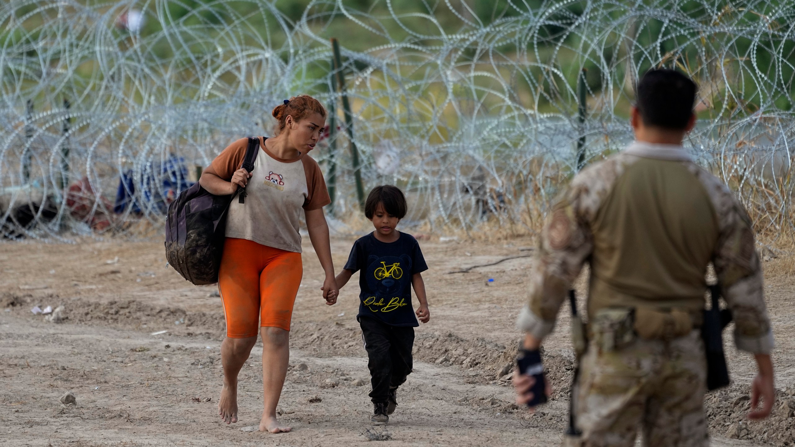 Migrants who crossed into the U.S. from Mexico walk past concertina wire lining the banks of the Rio Grande as they move to an area for processing, Sept. 21, 2023, in Eagle Pass, Texas. Migrants have always come to the U.S., but the immigration system now seems strained nationwide more than ever. (AP Photo/Eric Gay)