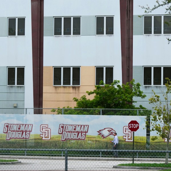 FILE - A security agent walks alongside a barrier surrounding Marjory Stoneman Douglas High School, July 5, 2023, in Parkland, Fla. Florida lawmakers and others on Saturday, Oct. 14, toured the school's 1200 Building, where a former student shot 17 people to death and wounded 17 others on Valentine's Day in 2018. The local school district has announced the 1200 Building will be demolished during the summer of 2024. (AP Photo/Rebecca Blackwell, File)