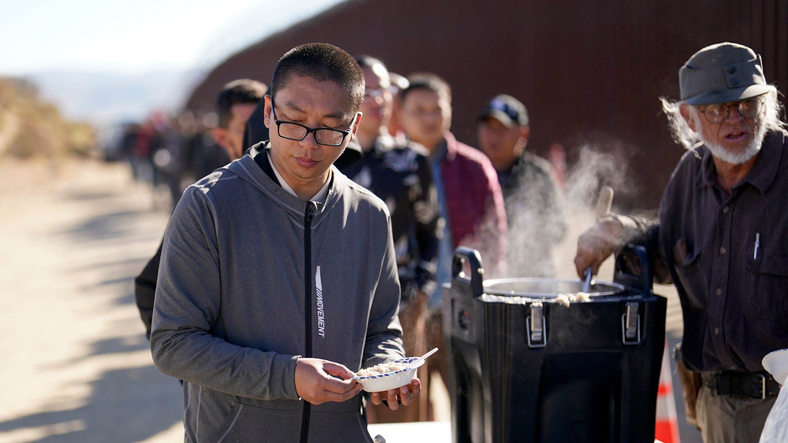 A man from China gets a bowl of oatmeal from a volunteer as he waits with others for processing to apply for asylum after crossing the border with Mexico, Tuesday, Oct. 24, 2023, near Jacumba, Calif. A major influx of Chinese migration to the United States on a relatively new and perilous route through Panama's Darién Gap jungle has become increasingly popular thanks to social media. (AP Photo/Gregory Bull)