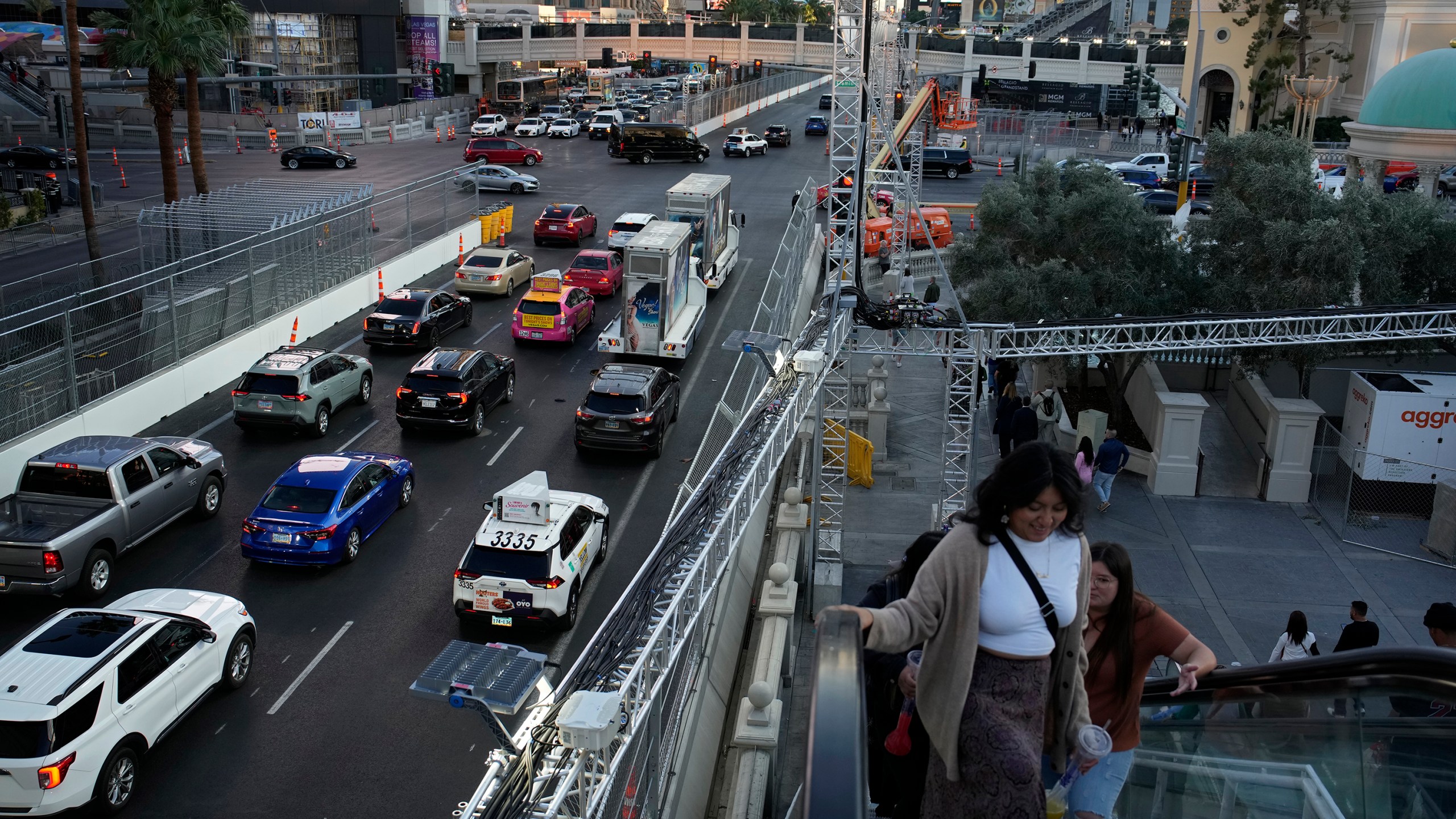 Pedestrians take an escalator along the Las Vegas Strip beside rigging and fencing installed ahead of the Las Vegas Formula One Grand Prix auto race Friday, Nov. 10, 2023, in Las Vegas. (AP Photo/John Locher)