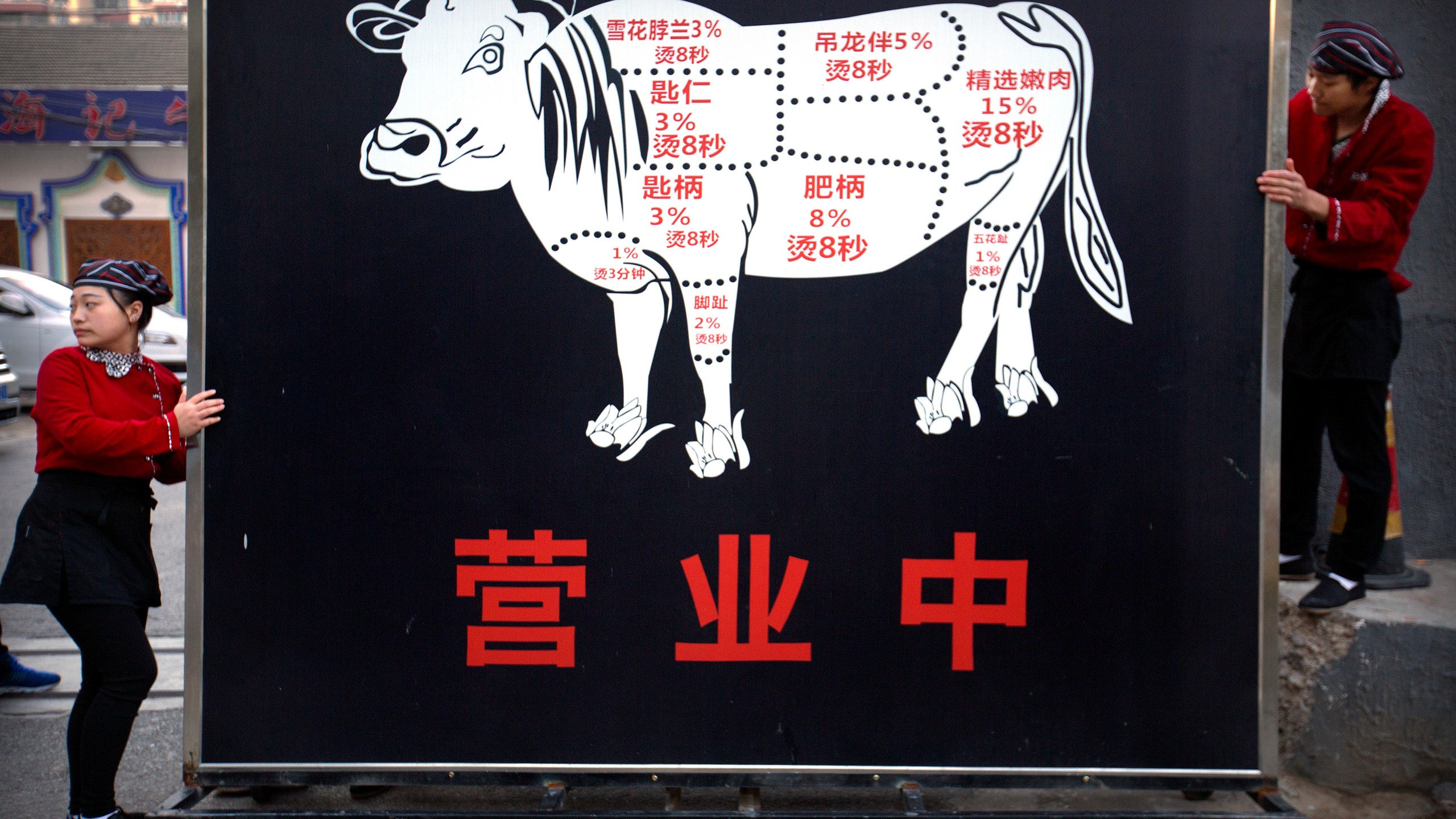 FILE - Restaurant workers move a sign advertising the grand opening of a beef hotpot restaurant along a street in Beijing, Thursday, Oct. 12, 2017. Experts agree that the urgency of climate change and the demands of a surging global population call for an overhaul of how humans get their protein. (AP Photo/Mark Schiefelbein, File)