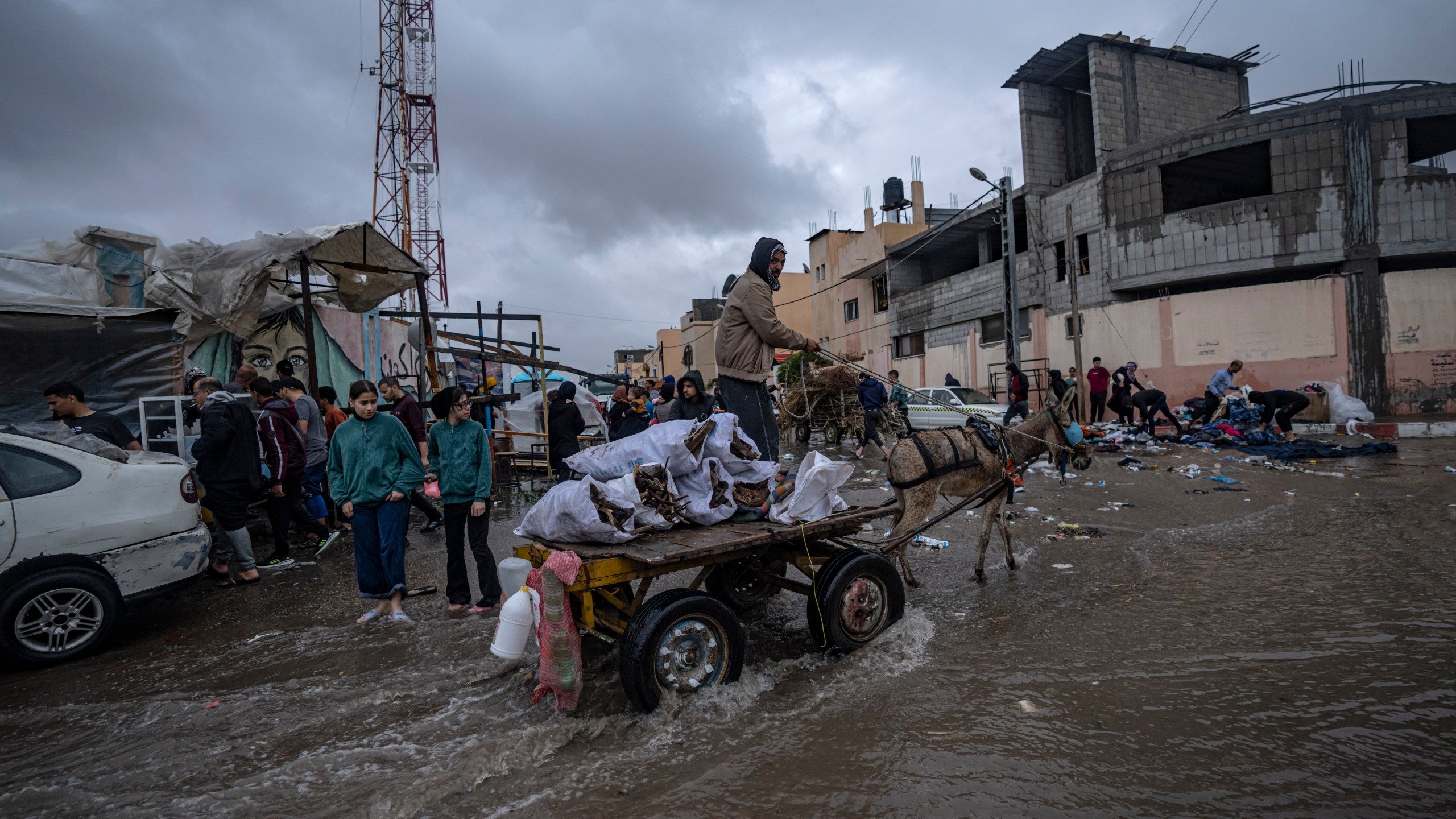 Palestinians displaced by the Israeli bombardment of the Gaza Strip walk through the flooded street after rainfall next to a U.N. displacement camp in the southern town of Khan Younis, Gaza Strip, Sunday, Nov. 19, 2023. Hundreds of thousands of Palestinians have fled their homes in northern Gaza as Israel moves ahead with a ground offensive against the ruling Hamas militant group. (AP Photo/Fatima Shbair)