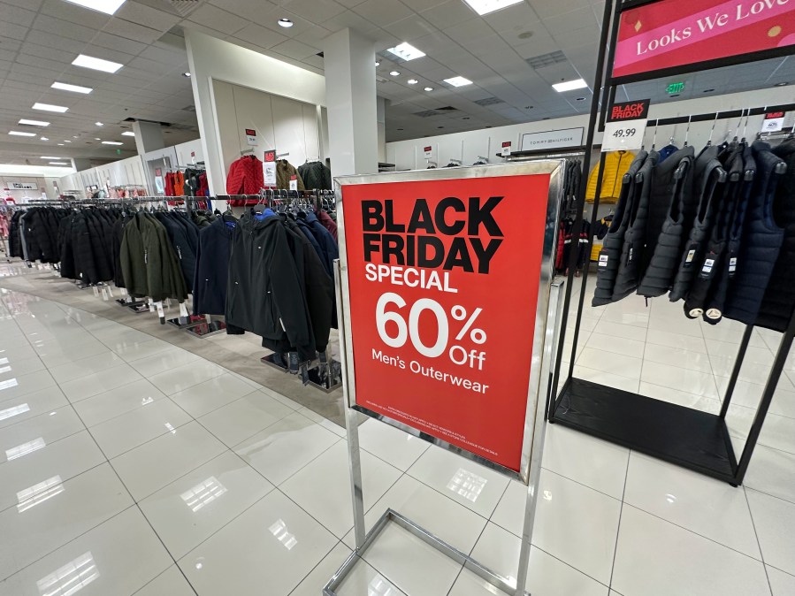 A sign notes Black Friday discount available on racks of men's outerwear in a Macy's department store on Monday, Nov. 20, 2023, in northeast Denver. While Black Friday may no longer look like the crowd-filled, in-person mayhem that it was just decades ago — in large part due to the rising dependence on online shopping that was accelerated by the COVID-19 pandemic — the holiday sales event is still slated to attract millions of consumers. (AP Photo/David Zalubowski)