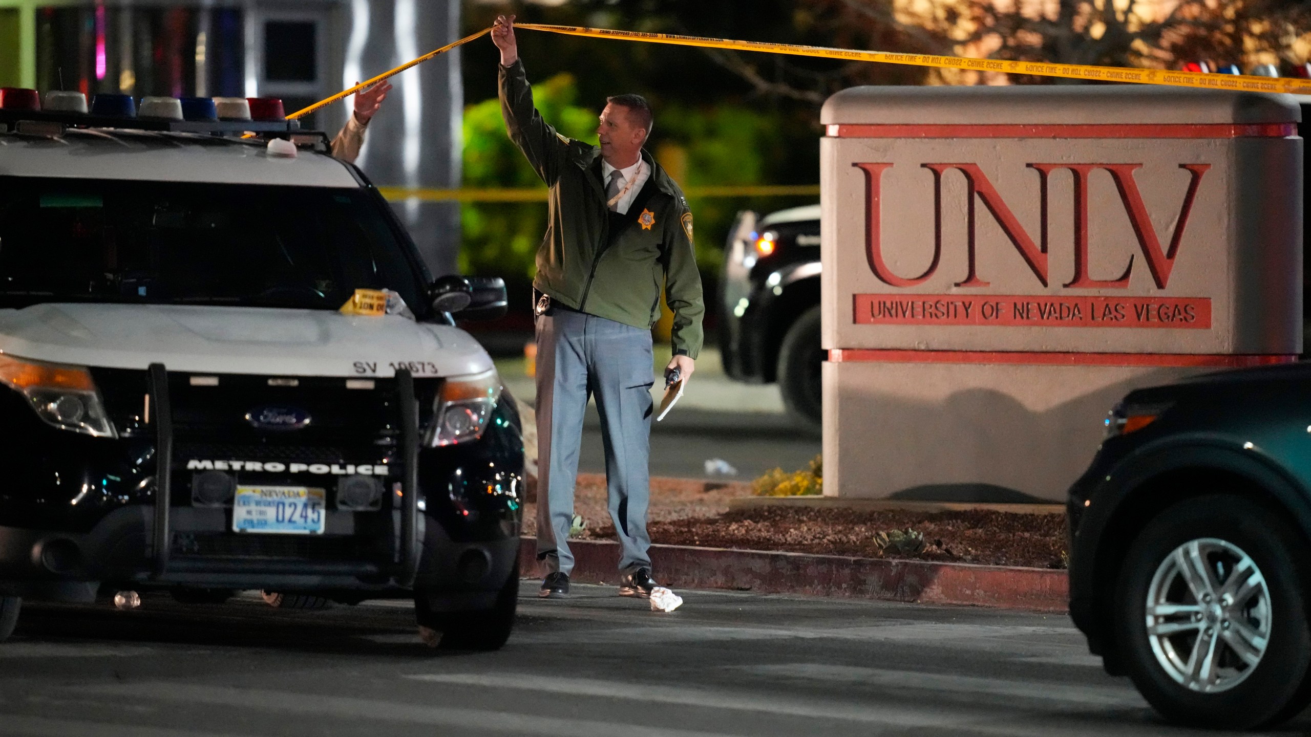 A police officer walks under crime scene tape in the aftermath of a shooting at the University of Nevada, Las Vegas, Wednesday, Dec. 6, 2023, in Las Vegas. (AP Photo/John Locher)