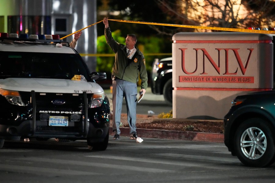 A police officer walks under crime scene tape in the aftermath of a shooting at the University of Nevada, Las Vegas, Wednesday, Dec. 6, 2023, in Las Vegas. (AP Photo/John Locher)