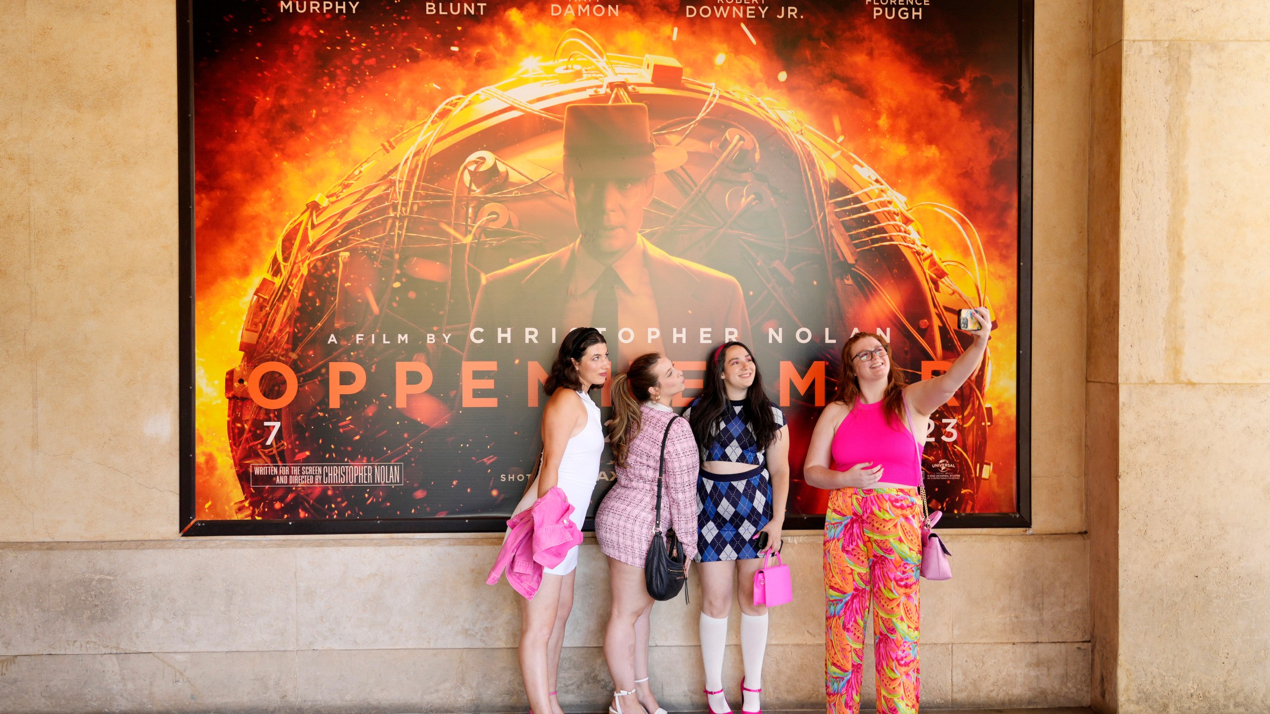 From left, Gabrielle Roitman, Kayla Seffing, Maddy Hiller and Casey Myer take a selfie in front of an "Oppenheimer" movie poster before they attended an advance screening of "Barbie," Thursday, July 20, 2023, at AMC The Grove 14 theaters in Los Angeles. (AP Photo/Chris Pizzello)