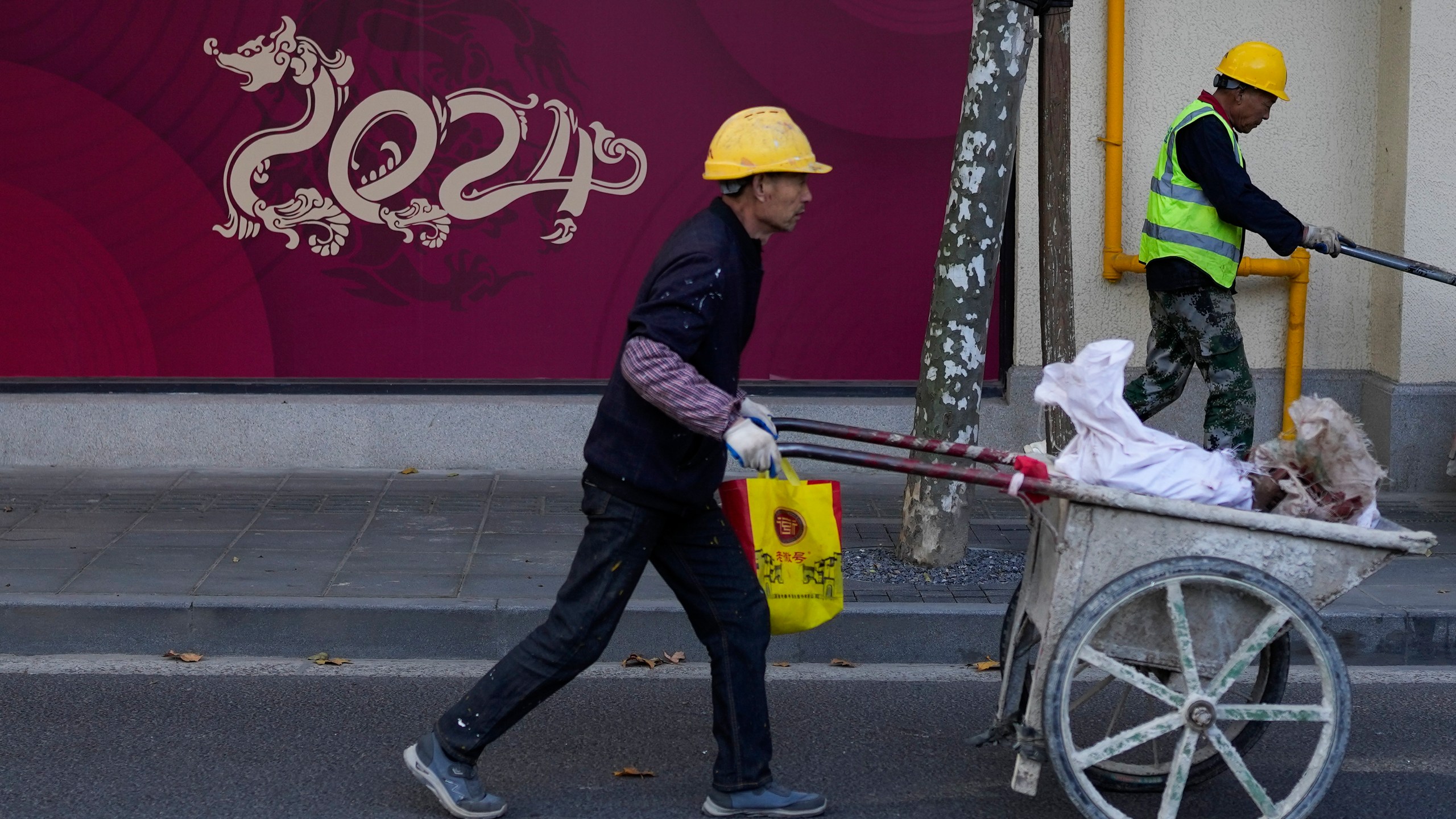 Workers push trolleys passing by under construction retail shop baring a dragon shaped 2024, the Year of the Dragon on the Chinese calendar, in Shanghai, China on Nov. 25, 2023. Chinese leaders have wrapped up a two-day annual meeting to set economic priorities for the coming year, the official Xinhua News Agency reported Tuesday, Dec. 12, 2023 without giving details of what was decided. (AP Photo/Andy Wong)