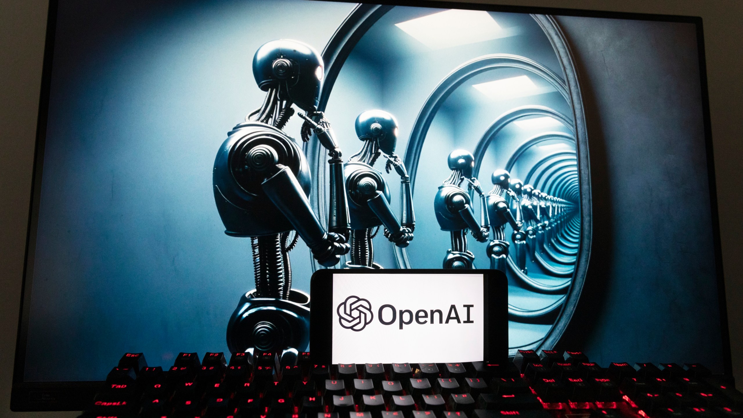 The OpenAI logo is seen displayed on a cell phone with an image on a computer screen generated by ChatGPT's Dall-E text-to-image model, Friday, Dec. 8, 2023, in Boston. Artificial intelligence went mainstream in 2023 — it was a long time coming and has a long way to go for the technology to match people's science fiction fantasies of human-like machines. (AP Photo/Michael Dwyer)