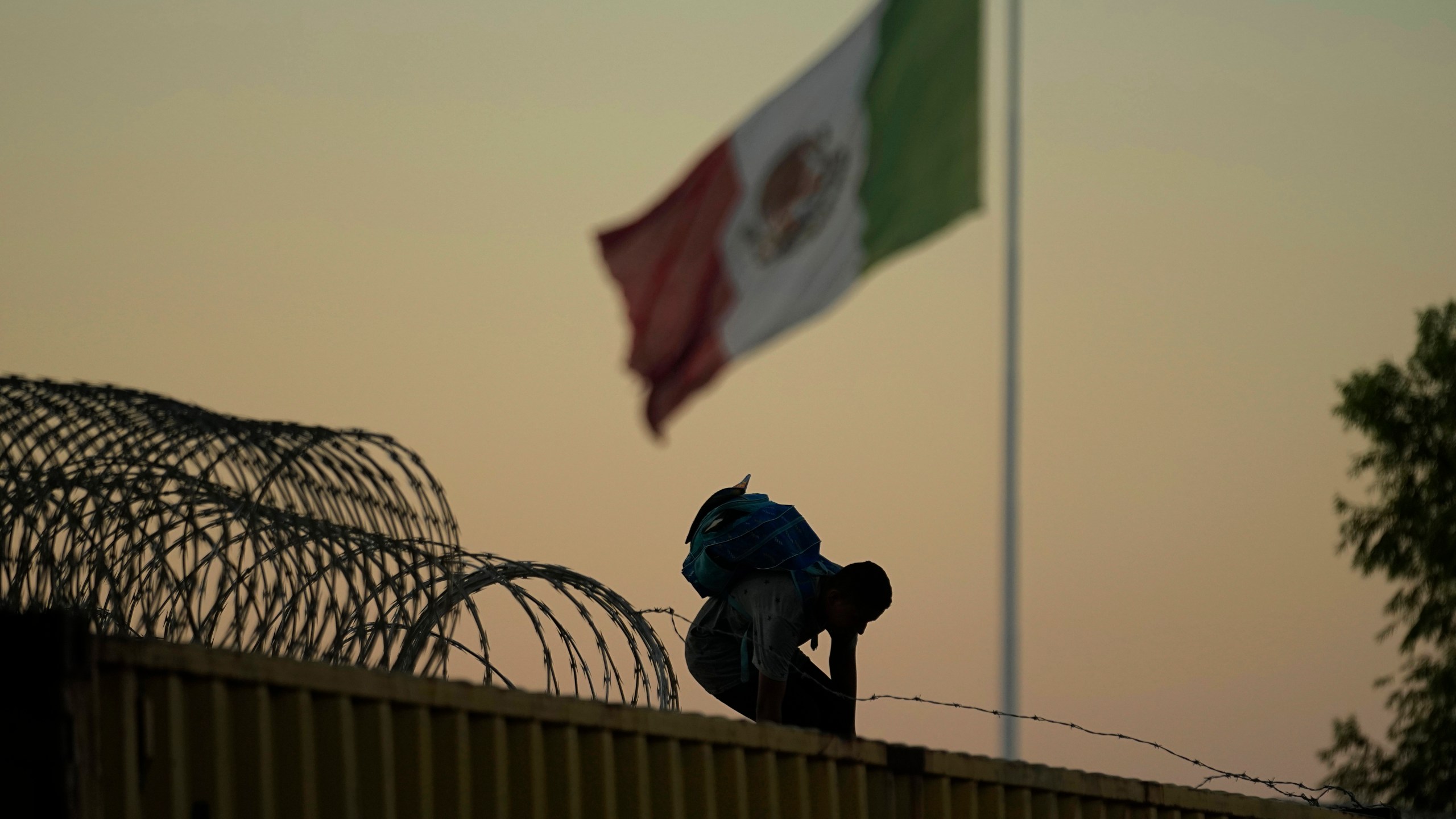 FILE - A migrant who crossed the Rio Grande from Mexico to the U.S. works their way through and over concertina wire and box car barriers, Friday, Sept. 22, 2023, in Eagle Pass, Texas. Abbott is expected to sign into law sweeping new powers that allow police to arrest migrants who cross the border illegally and gives local judges authority to order them to leave the country.(AP Photo/Eric Gay, File)