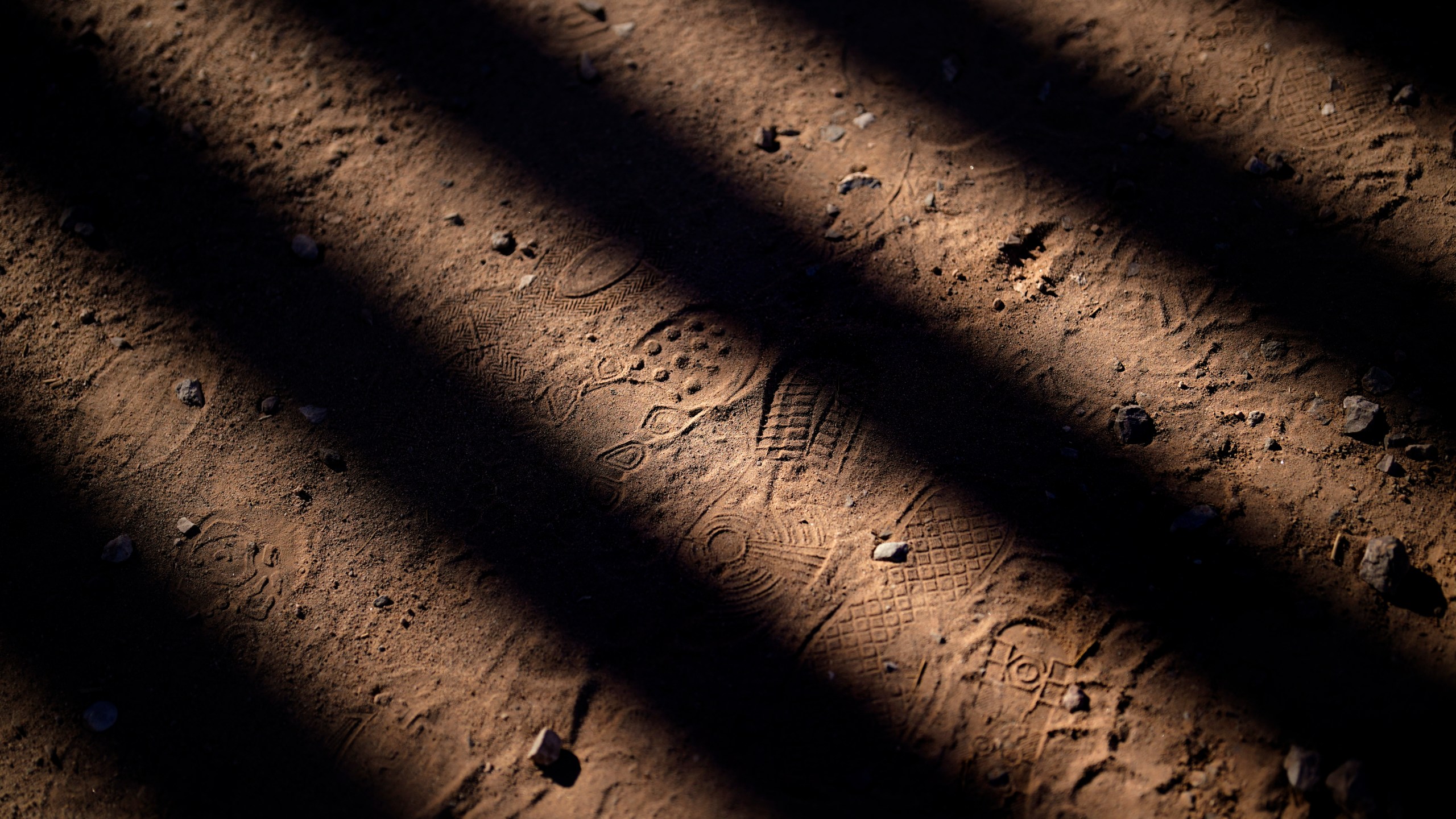 FILE - Footsteps are seen along a road shadowed by the steel columns of the border wall separating Arizona and Mexico, Friday, Dec. 15, 2023, near Lukeville, Ariz. (AP Photo/Gregory Bull, File)