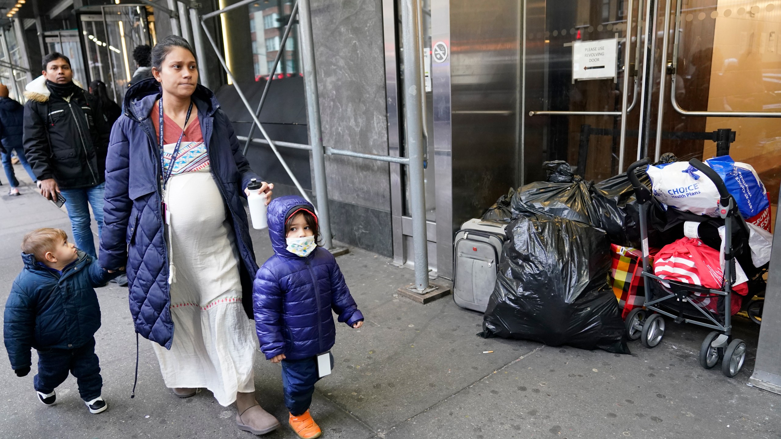 A pregnant woman and children who left the Row Hotel walk past the belongings of other immigrants, Tuesday, Jan. 9, 2024, in New York. (AP Photo/Mary Altaffer)