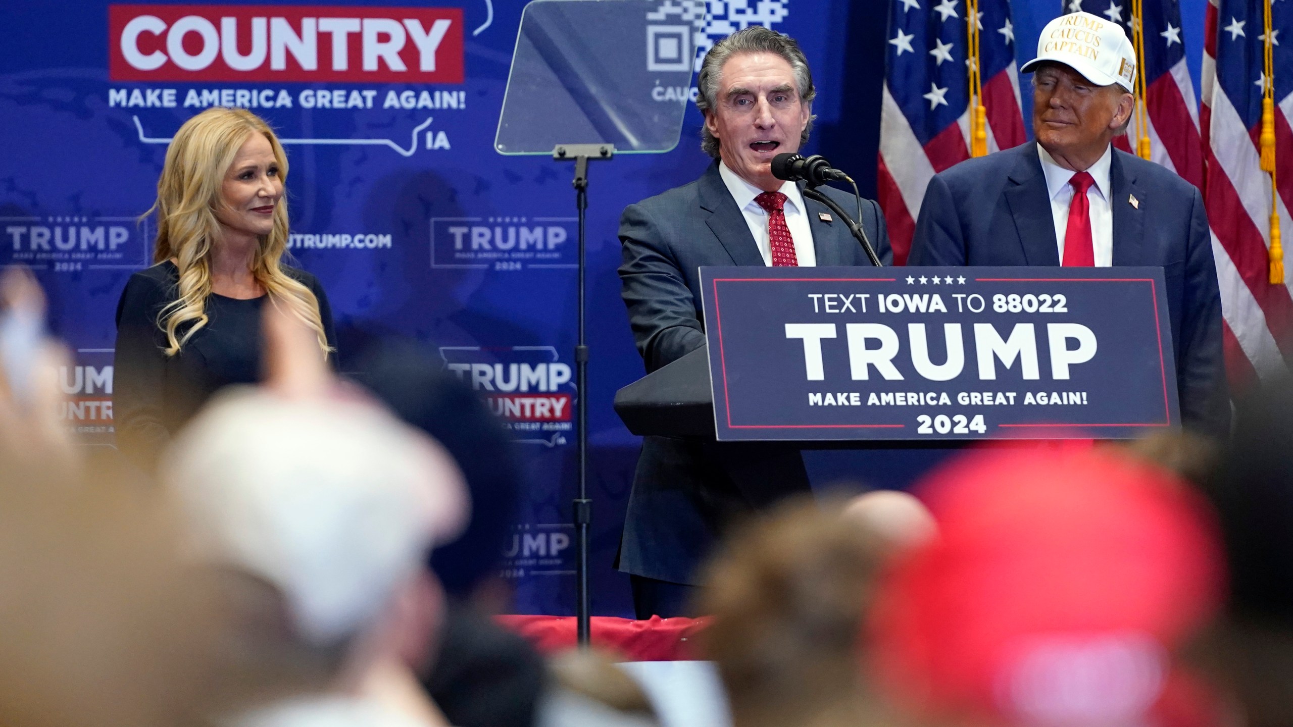 Republican presidential candidate former President Donald Trump listens as North Dakota Gov. Doug Burgum speaks at a rally at Simpson College in Indianola, Iowa, Sunday, Jan. 14, 2024. At left is Kathryn Burgum. (AP Photo/Andrew Harnik)