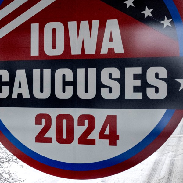 A man walks across the street below a sign for the Iowa Caucuses in downtown Des Moines, Iowa, Saturday, Jan. 13, 2024. (AP Photo/Andrew Harnik)