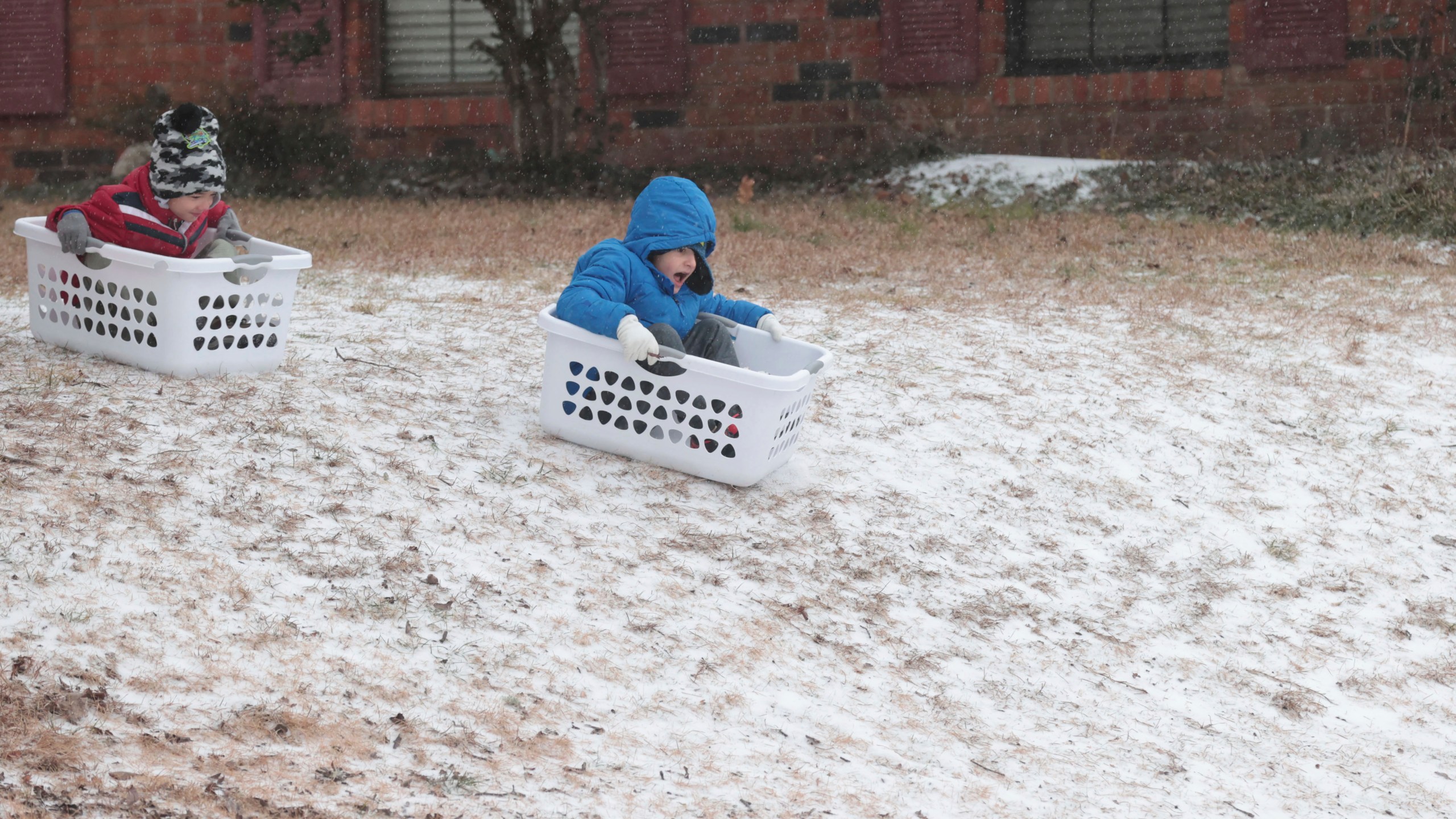 Cannon Lambert, 6, left, and Edward Nahar, 7, race down a hill using laundry baskets for sleds, Monday, Jan. 15, 2024, in Tupelo, Miss., as they enjoy the snowy conditions. (Thomas Wells/The Northeast Mississippi Daily Journal via AP)