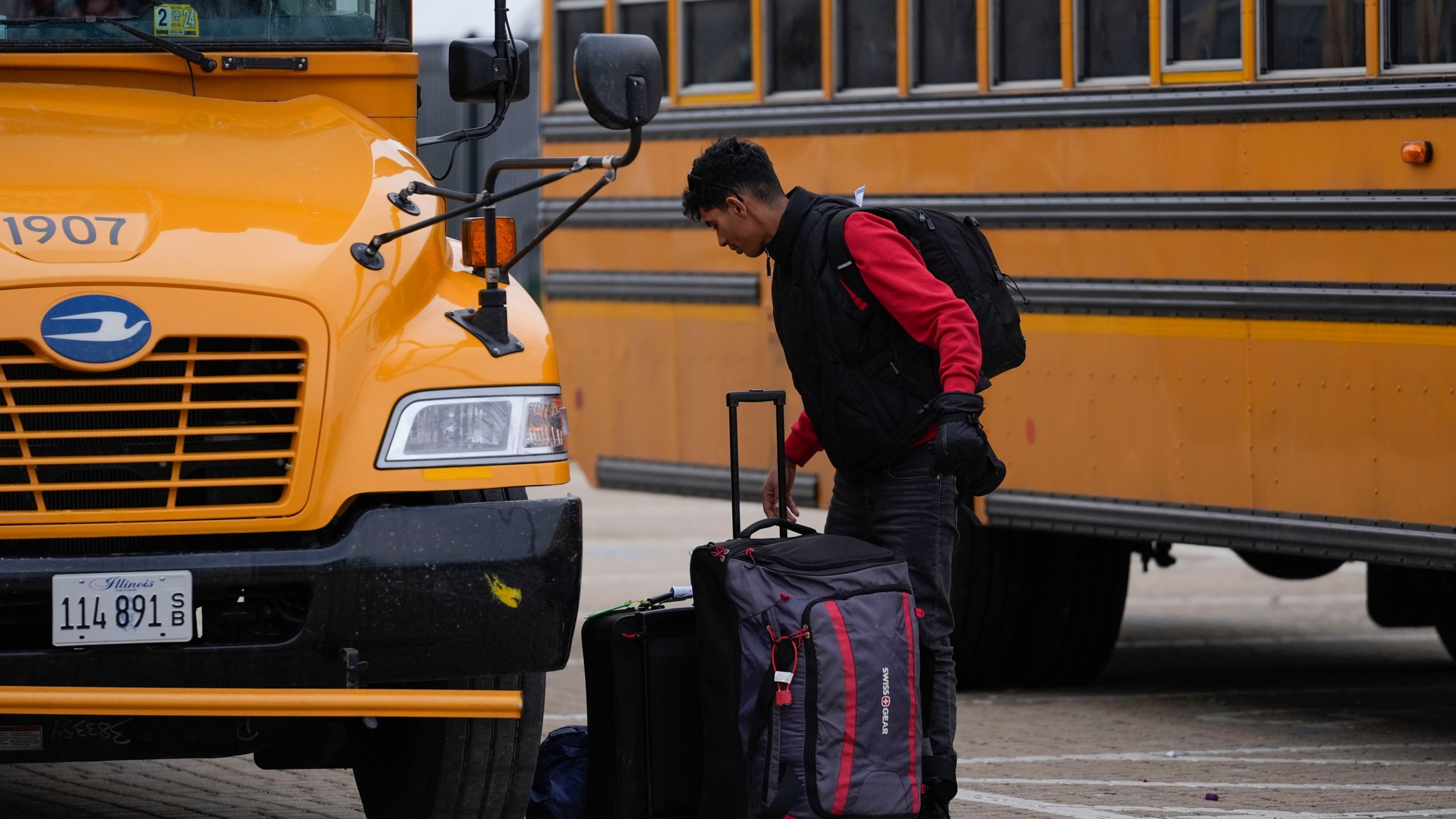 An arriving migrant departs a school bus in the 800 block of South Desplaines Street where Chicago Transit Authority "warming" buses for migrants are parked Thursday, Jan. 11, 2024, in Chicago. In the city of Chicago's latest attempt to provide shelter to incoming migrants, several buses were parked in the area to house people in cold winter weather. (AP Photo/Erin Hooley)