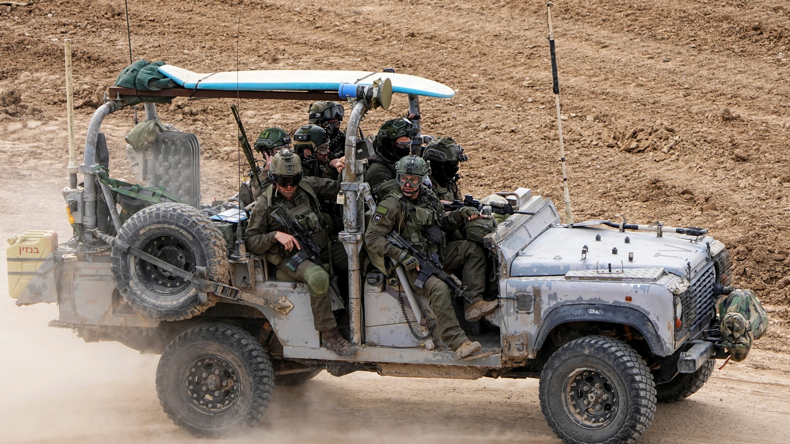 Israeli soldiers with a surfboard on the roof of their vehicle drive towards the Gaza Strip, in southern Israel, Tuesday, Feb. 13, 2024. The army is battling Palestinian militants across Gaza in the war ignited by Hamas' Oct. 7 attack into Israel. (AP Photo/Ariel Schalit)