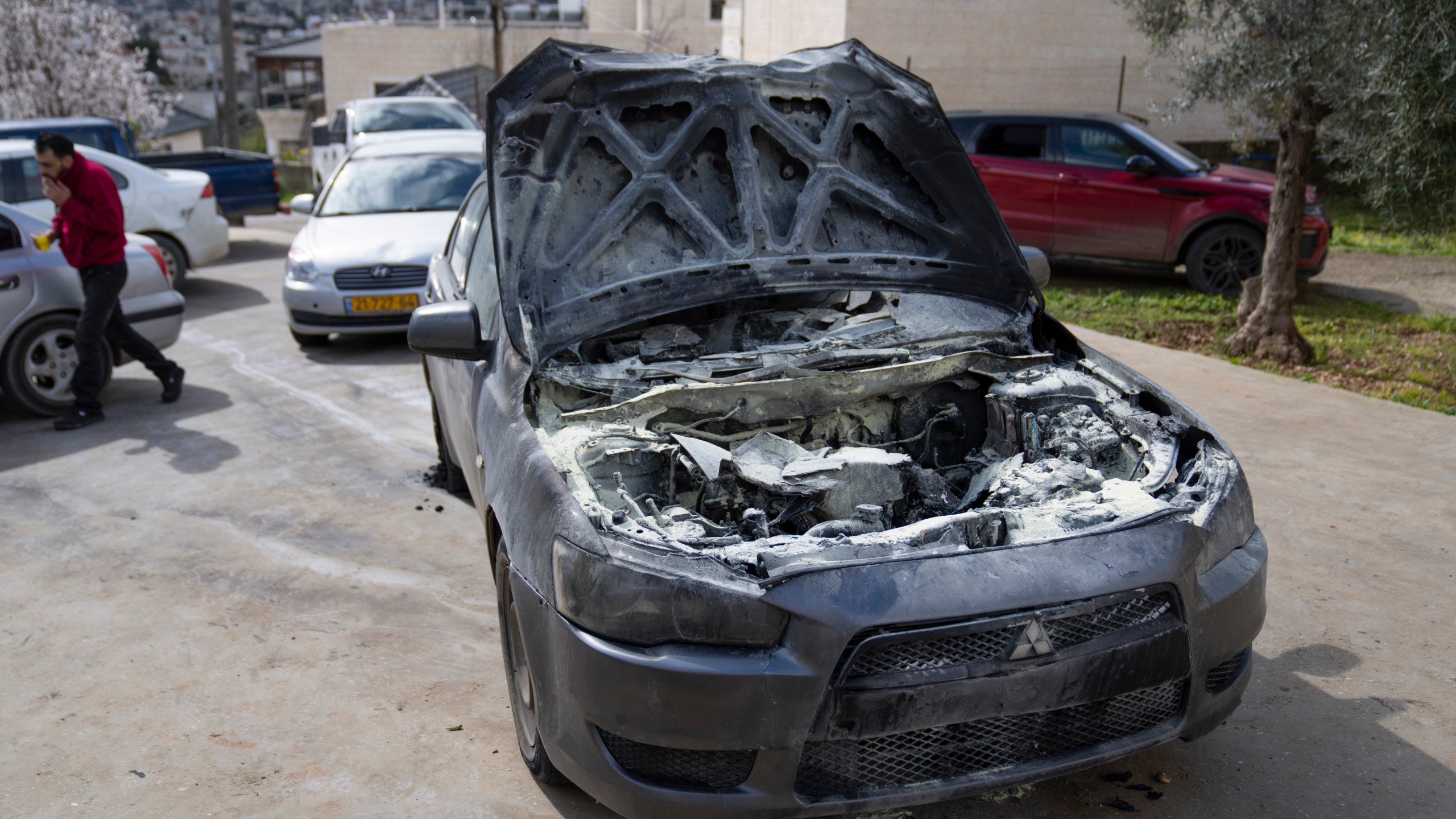 A man walks past a vehicle allegedly set ablaze by Jewish West Bank settlers in the Palestinian West Bank village of Turmus Ayya, Sunday, Feb. 18, 2024. Village residents claimed that settlers raided the outskirts of the village overnight, setting fire to a car and spaying graffiti on the walls of homes. (AP Photo/Nasser Nasser)