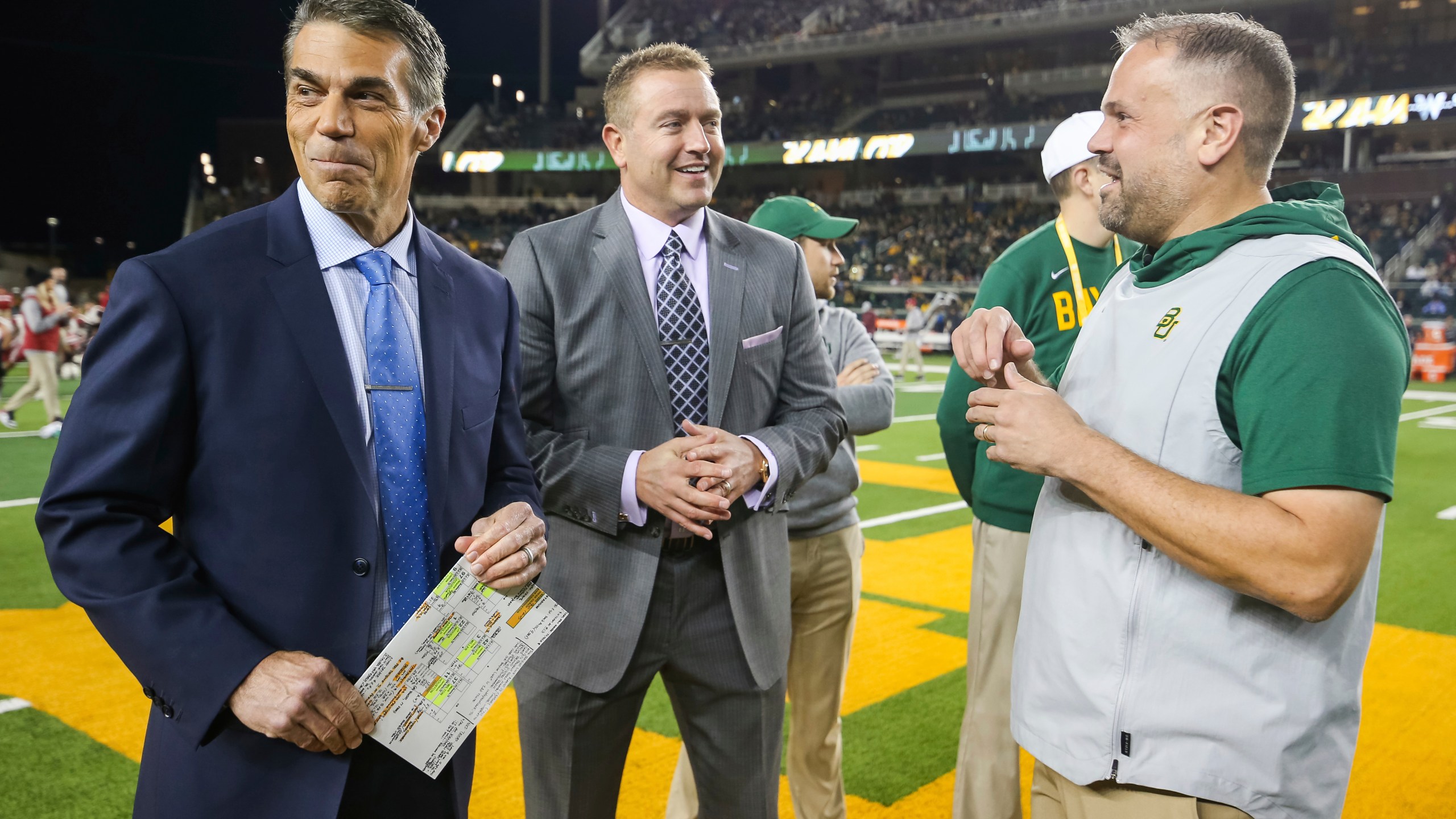 ESPN's Chris Fowler, left, and Kirk Herbstreit, center, talk with Baylor head coach Matt Rhule prior to an NCAA college football game against Oklahoma in Waco, Texas, Saturday, Nov. 16, 2019. The ESPN “College GameDay” analyst Herbstreit and the network's broadcaster Fowler announced Thursday, Feb. 22, 2024, on social media they will be voices in EA Sports' upcoming college football video game. (AP Photo/Ray Carlin, File)