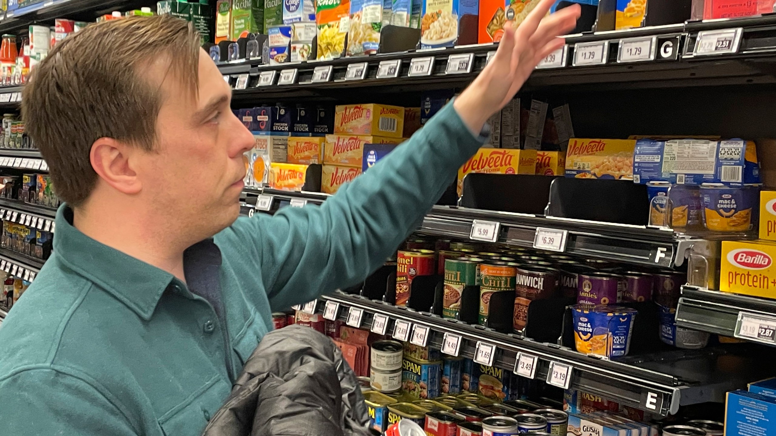 Stuart Dryden reaches for an item at a grocery store on Wednesday, Feb. 21, 2024, in Arlington, Va. Dryden is aware of big price disparities between branded products and their store-label competitors, which he now favors. (AP Photo/Chris Rugaber)