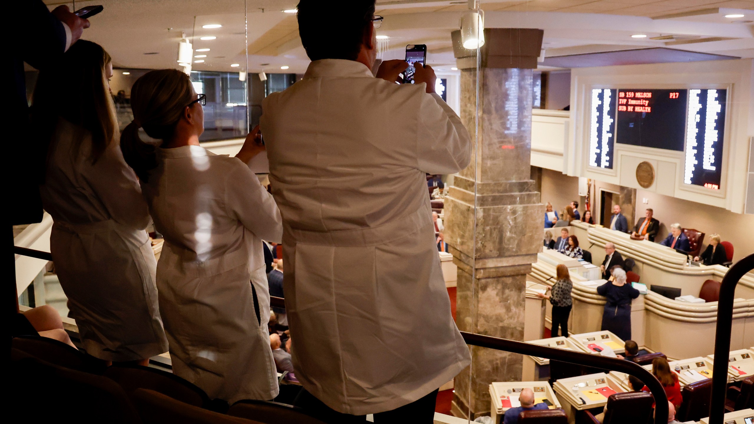 Doctors from the Alabama Fertility Clinic takes photos of the votes as the debate over SB159 bill (IVF Fertility Bill) in the House Chambers is voted on, Wednesday, March 6, 2024, in Montgomery, Ala. (AP Photo/ Butch Dill)