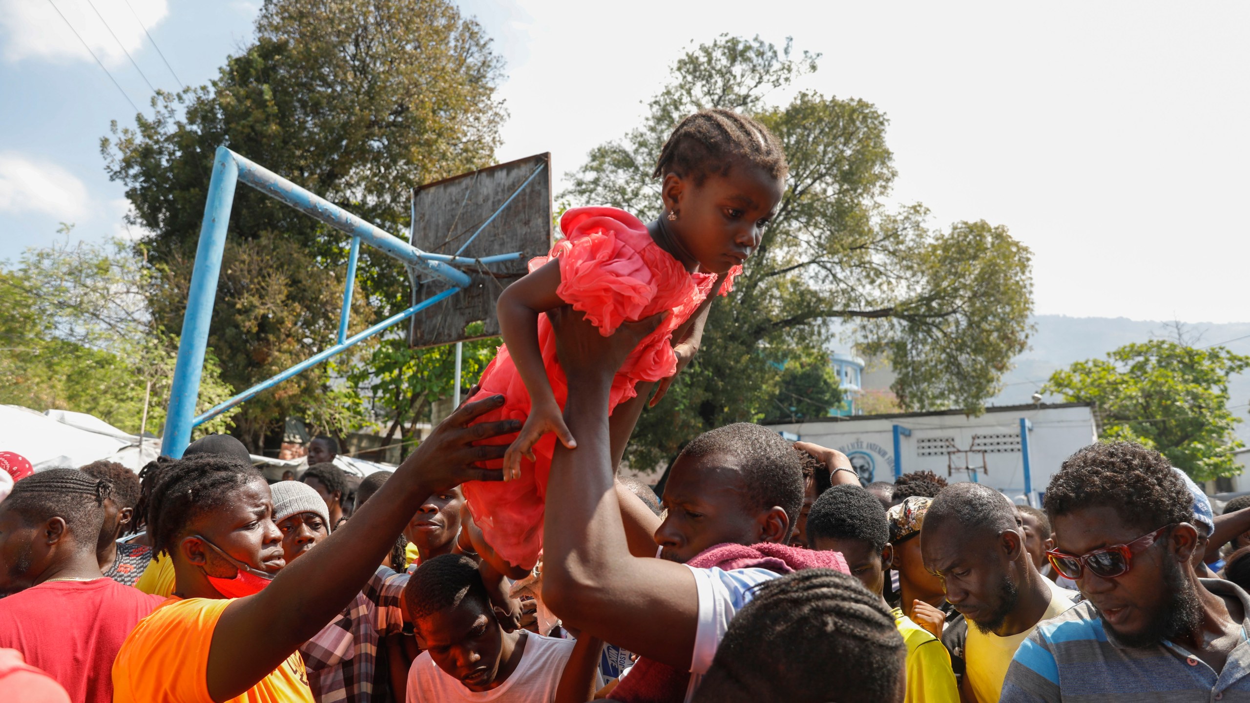 A father lifts his daughter to the front of a line of people waiting to receive a plate of food, at a shelter for families displaced by gang violence in Port-au-Prince, Haiti, Thursday, March 14, 2024. (AP Photo/Odelyn Joseph)