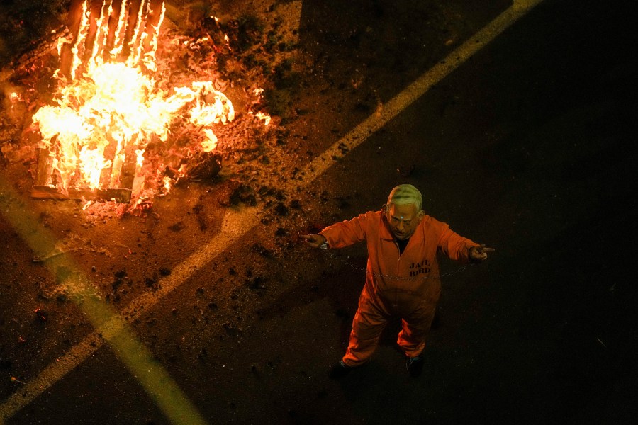 A demonstrator wearing a mask depicting Israeli Prime Minister Benjamin Netanyahu in a prisoner uniform blocks a road during a protest against Netanyahu's government and call for the release of hostages held in the Gaza Strip by the Hamas militant group, in Tel Aviv, Israel, Saturday, March 23, 2024. (AP Photo/Ariel Schalit)